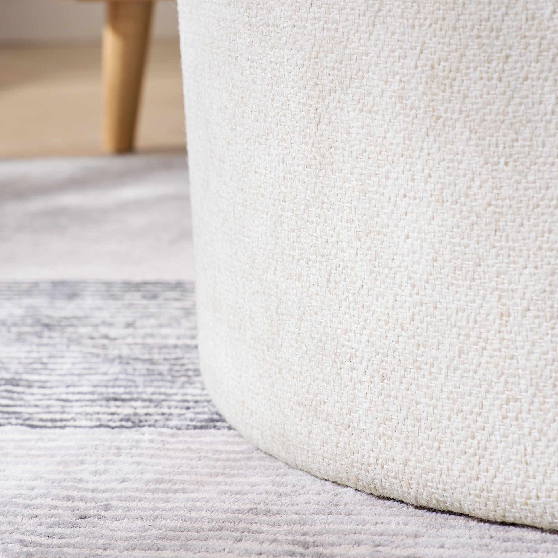 Closeup of a textured cream fabric ottoman with wooden legs part of a living room setup