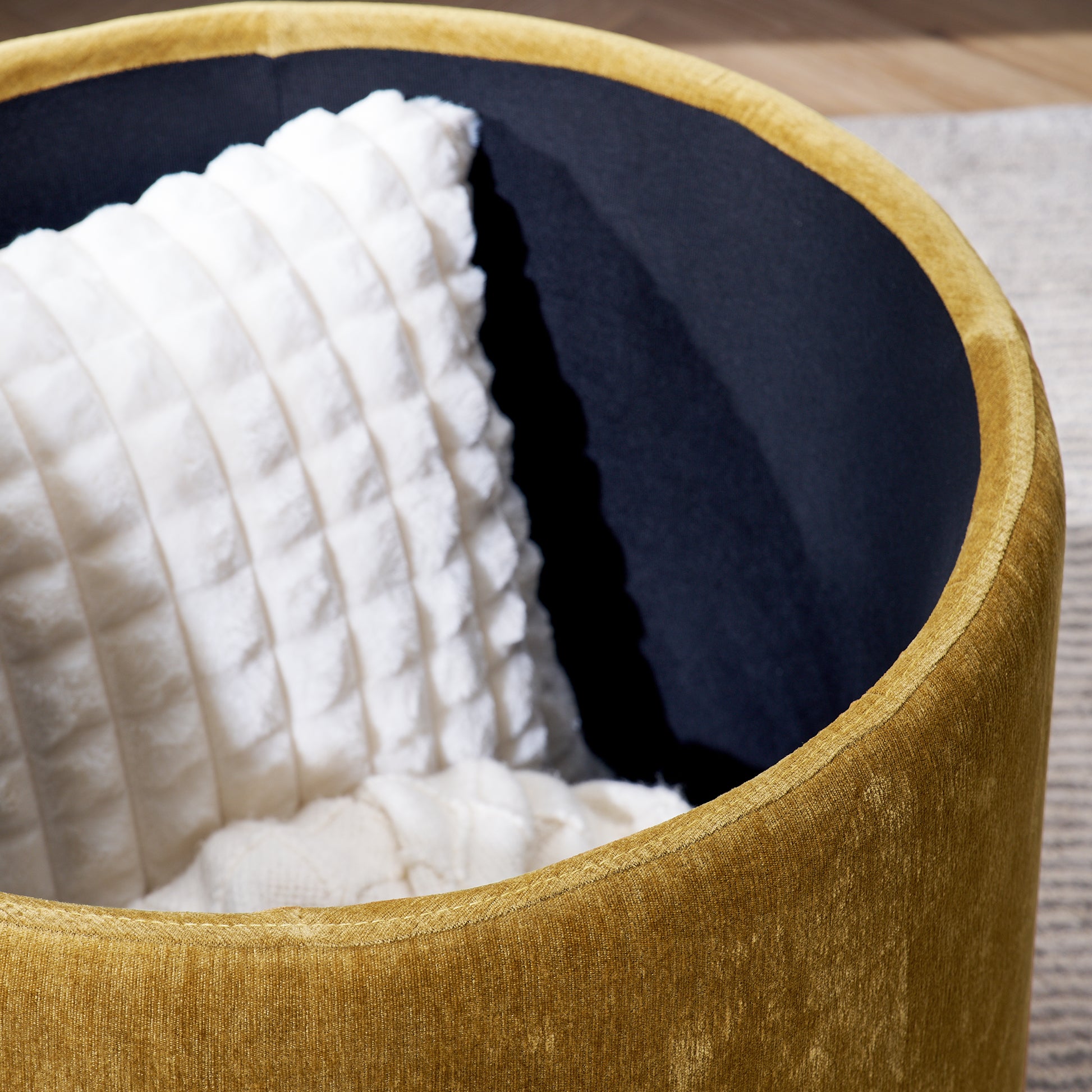 Gold velvet round ottoman with dark navy interior and plush white throw pillow