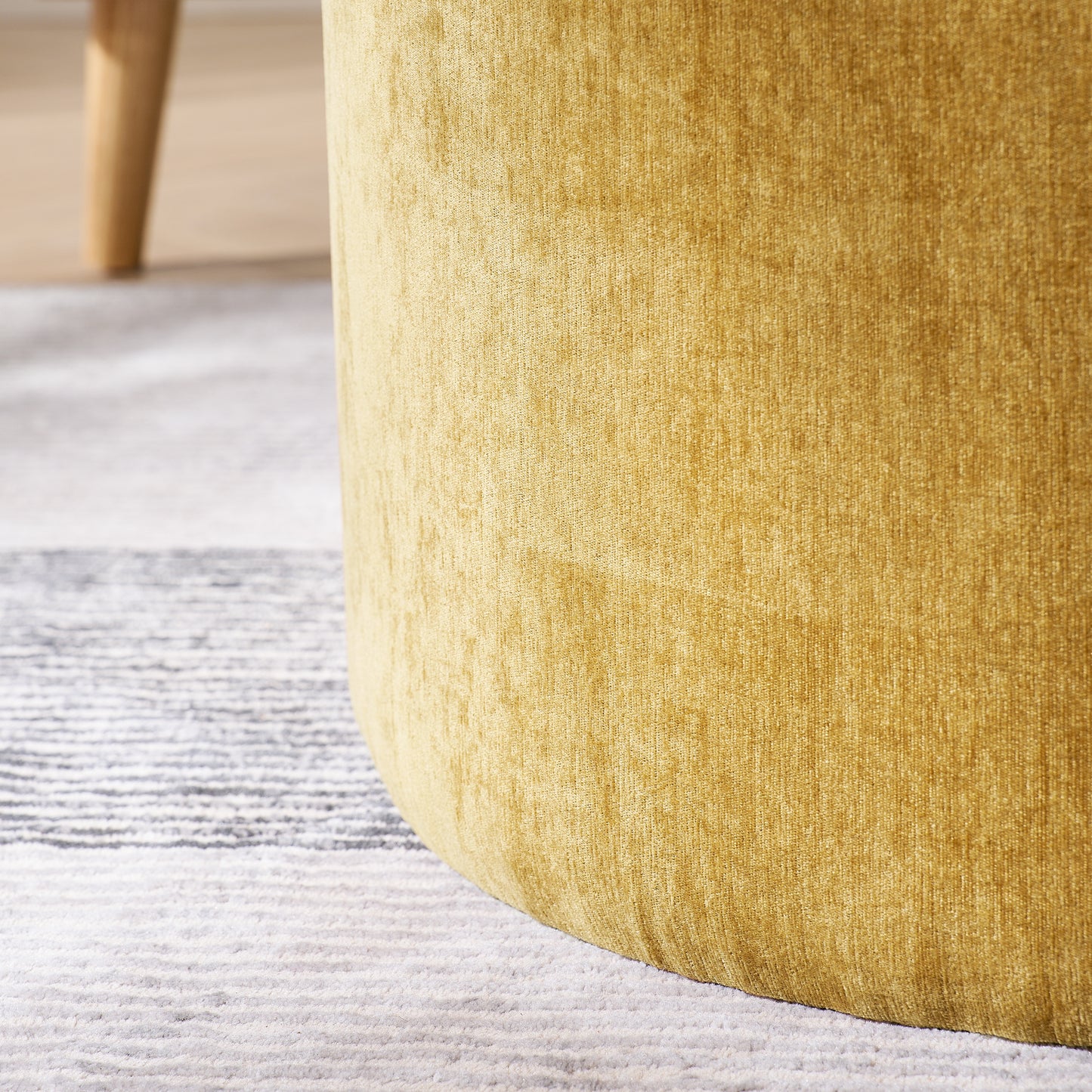Closeup of a textured mustard yellow velvet ottoman with wooden legs on a grey rug