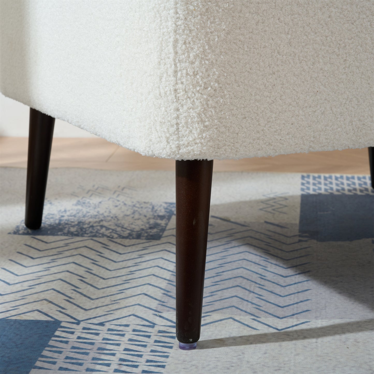 Closeup of a white boucle armchair leg accentuating its textured fabric upholstery and dark wood tapered leg
