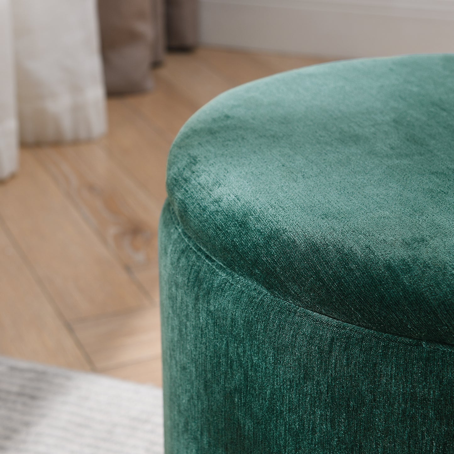 Deep emerald green velvet round ottoman with textured fabric surface