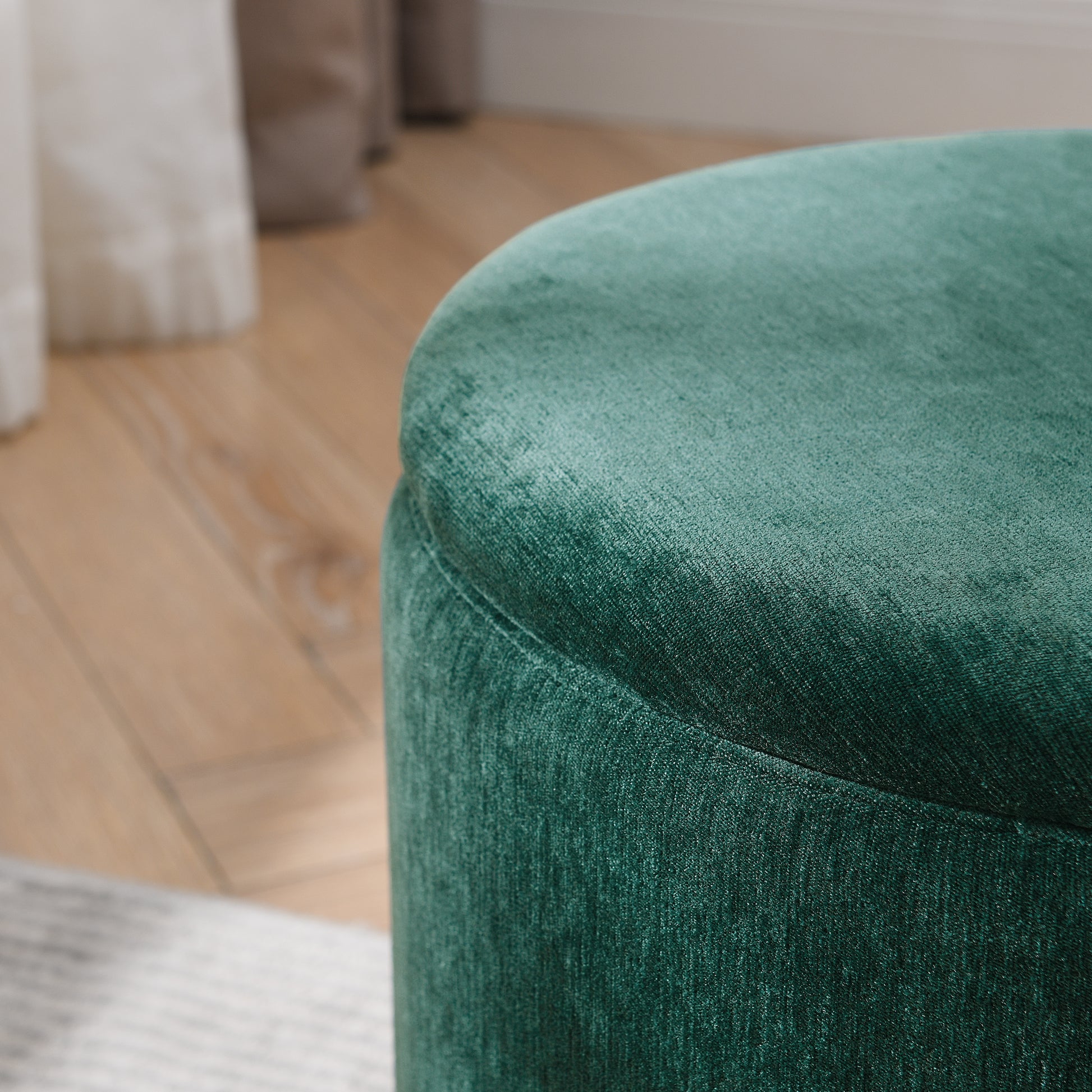 Deep emerald green velvet round ottoman with textured fabric surface