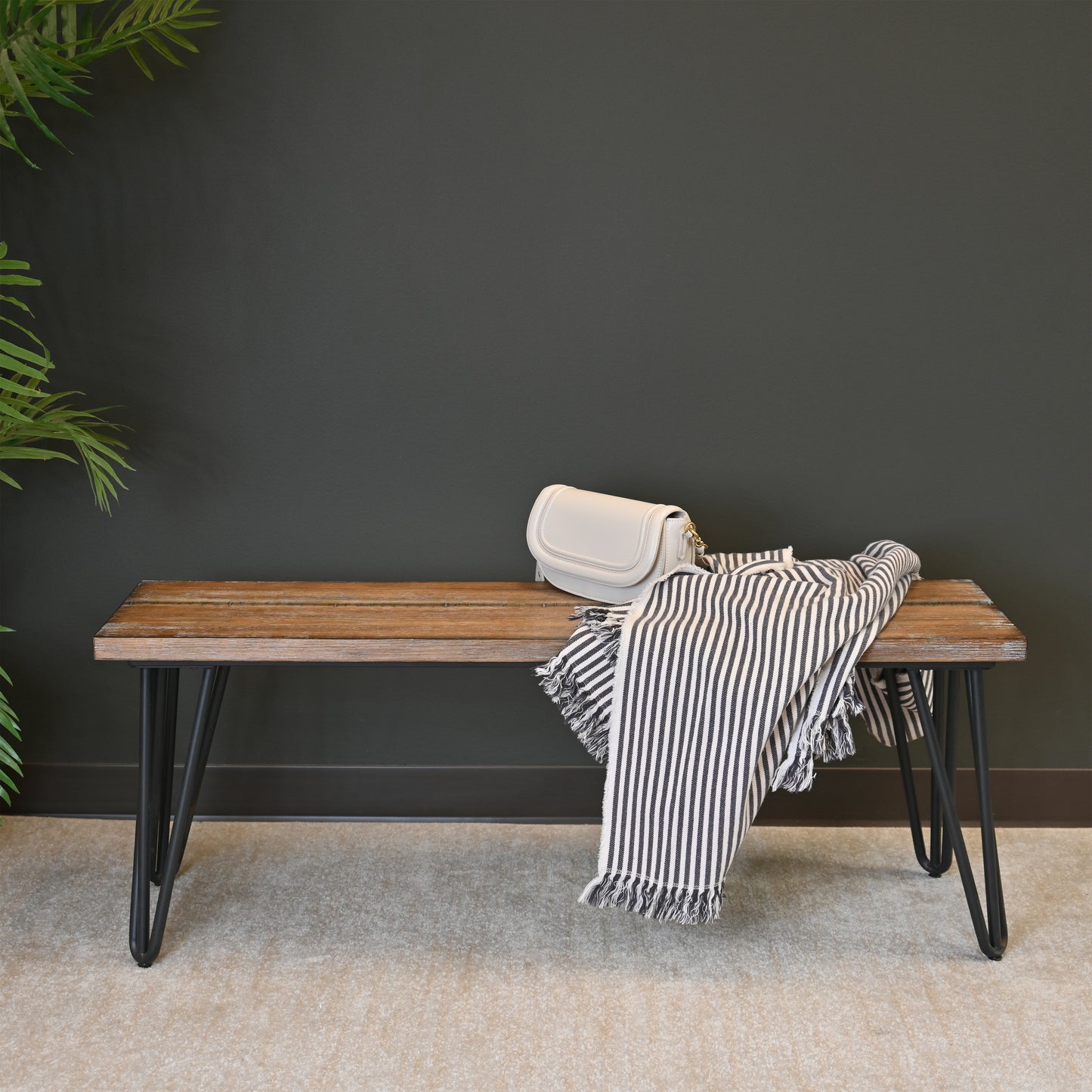 Rustic wooden bench with hairpin legs displaying a white handbag and striped throw