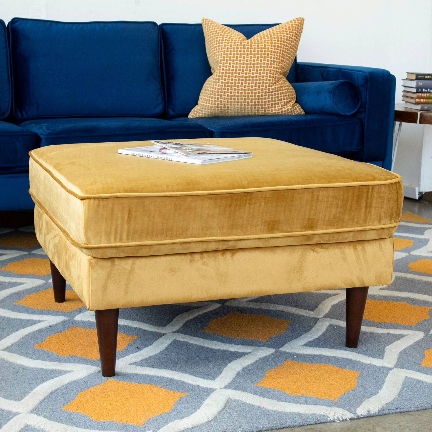 Plush velvet mustard ottoman with tapered wooden legs complementing modern living rooms