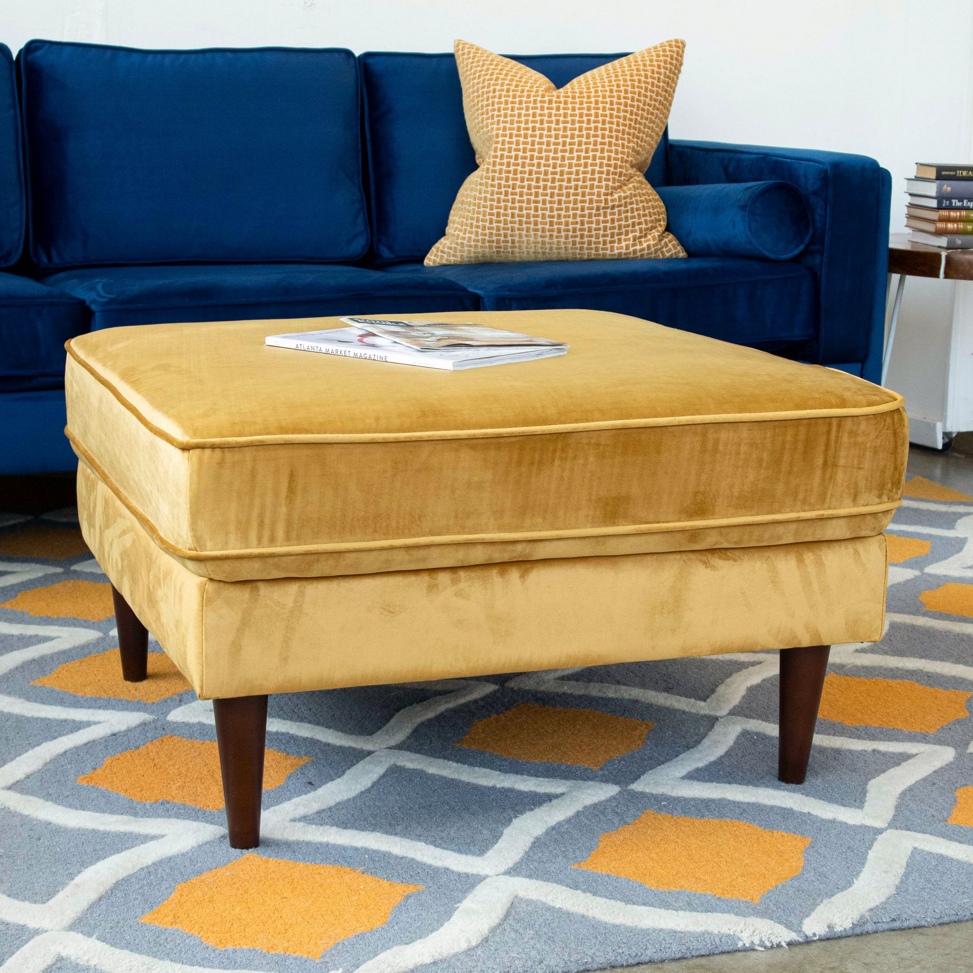 Plush velvet mustard ottoman with tapered wooden legs complementing modern living rooms