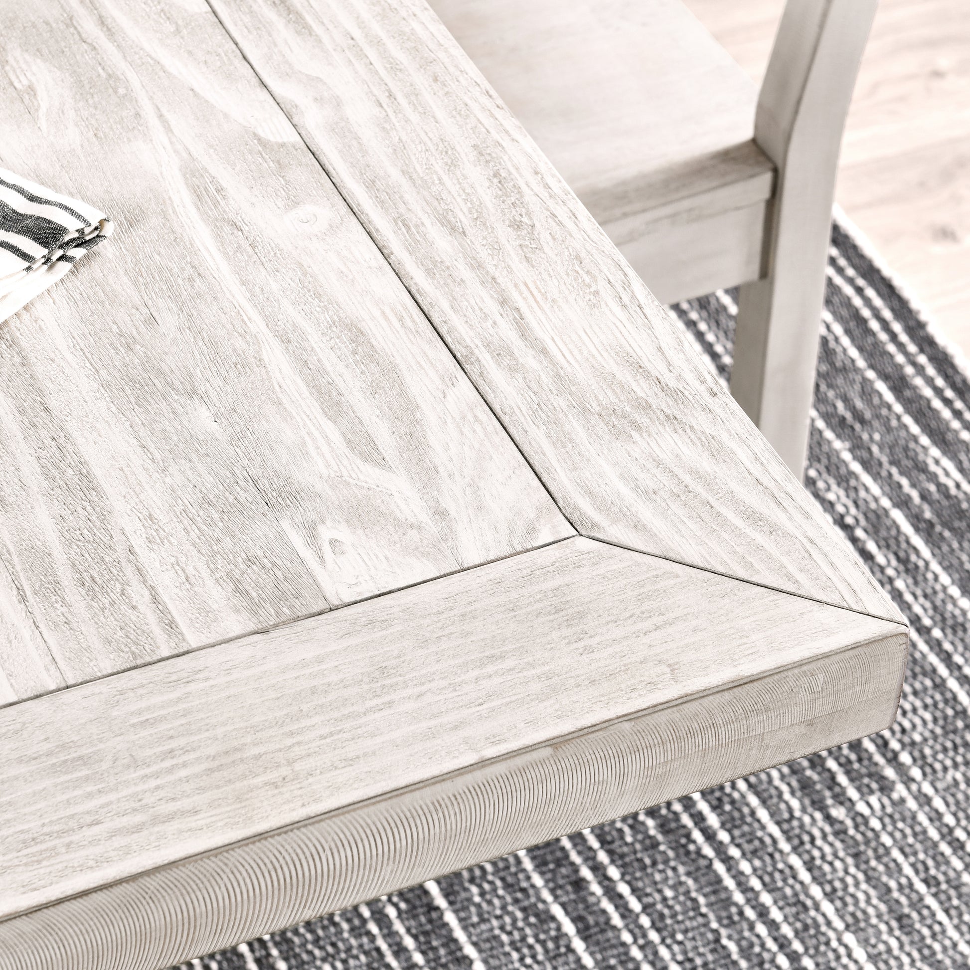 Closeup of a weathered white wood dining table with visible grain and a striped napkin