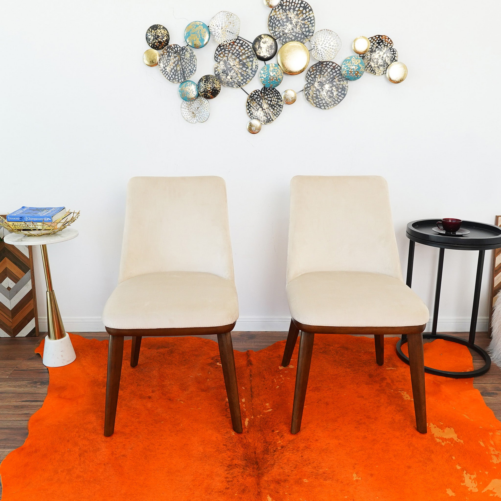 Two cream velvet accent chairs with dark wood legs on an orange cowhide rug