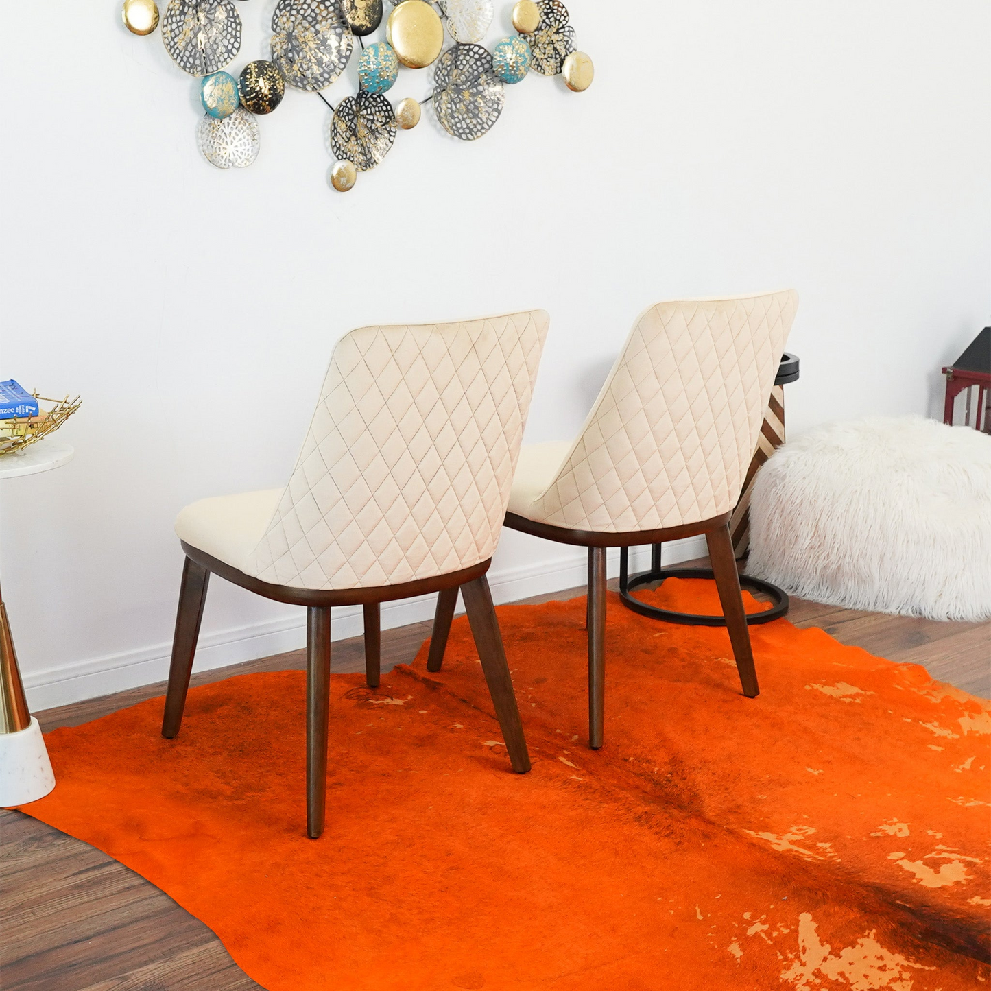 Two diamondtufted cream upholstered dining chairs with dark wood legs on an orange hide rug