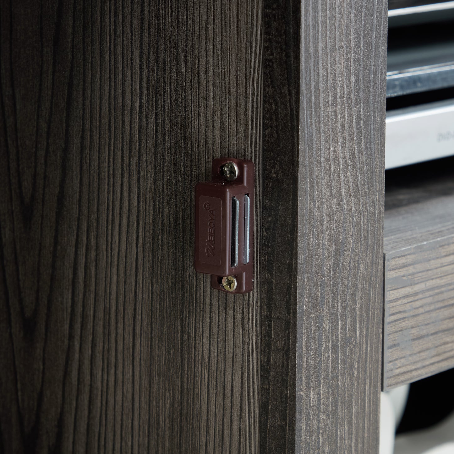 Closeup of a dark wood grain cabinet door with a brown magnetic catch attached via a screw