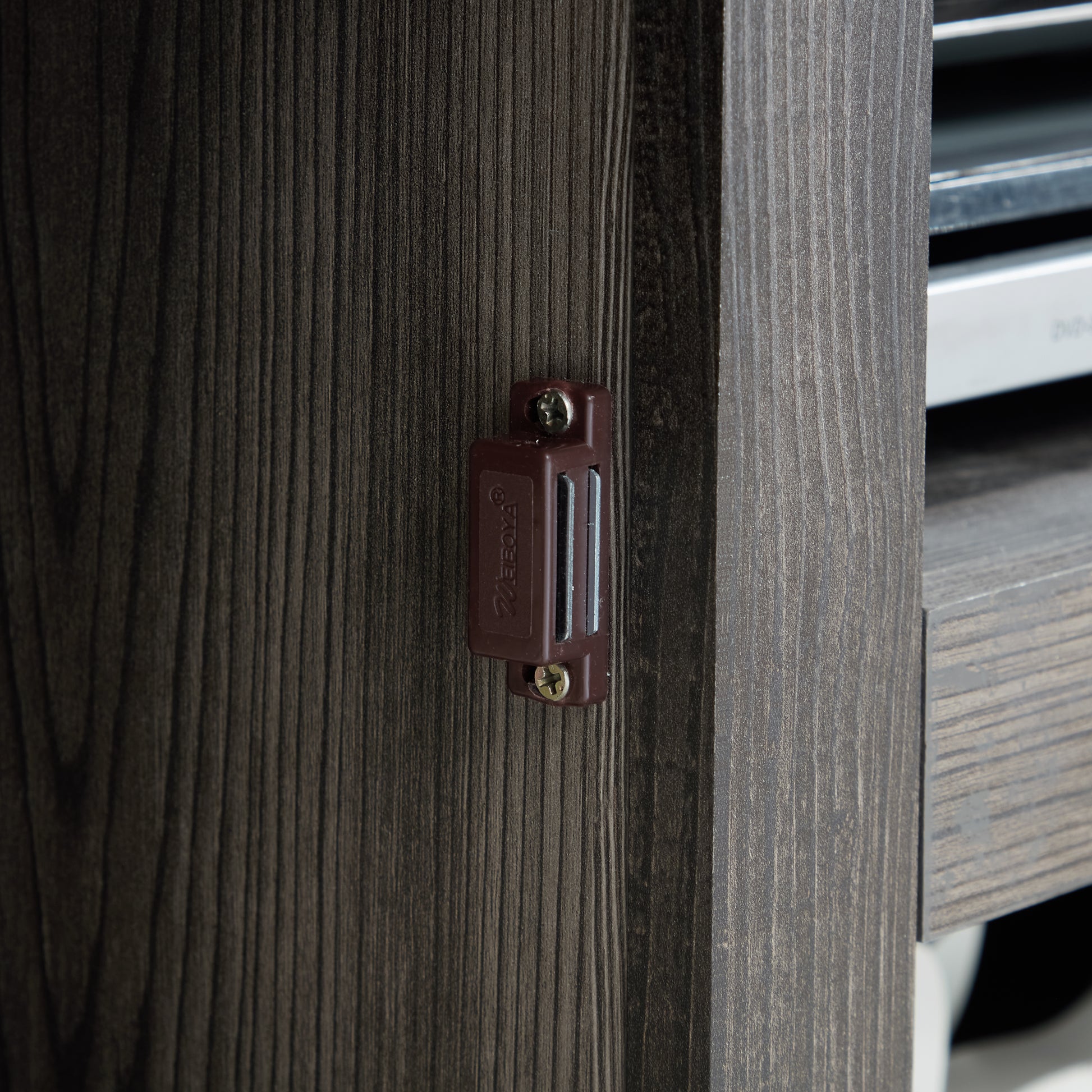 Closeup of a dark wood grain cabinet door with a brown magnetic catch attached via a screw