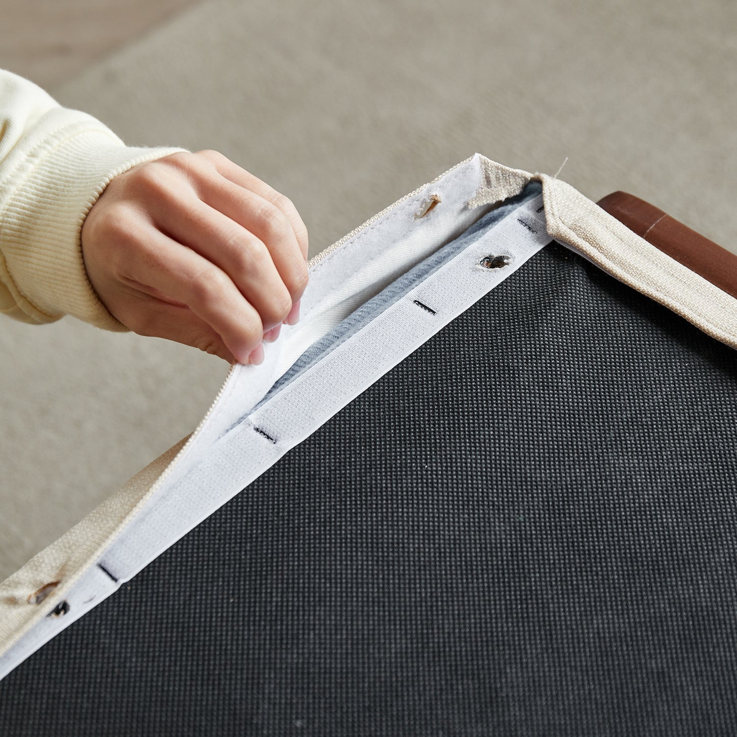 Closeup of a hand pulling a beige fabric cover with Velcro from a dark textured cushion