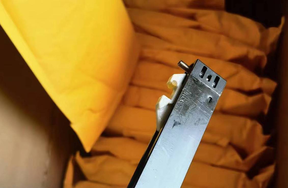Silver metal bracket with screw and white clip next to yellow packaging