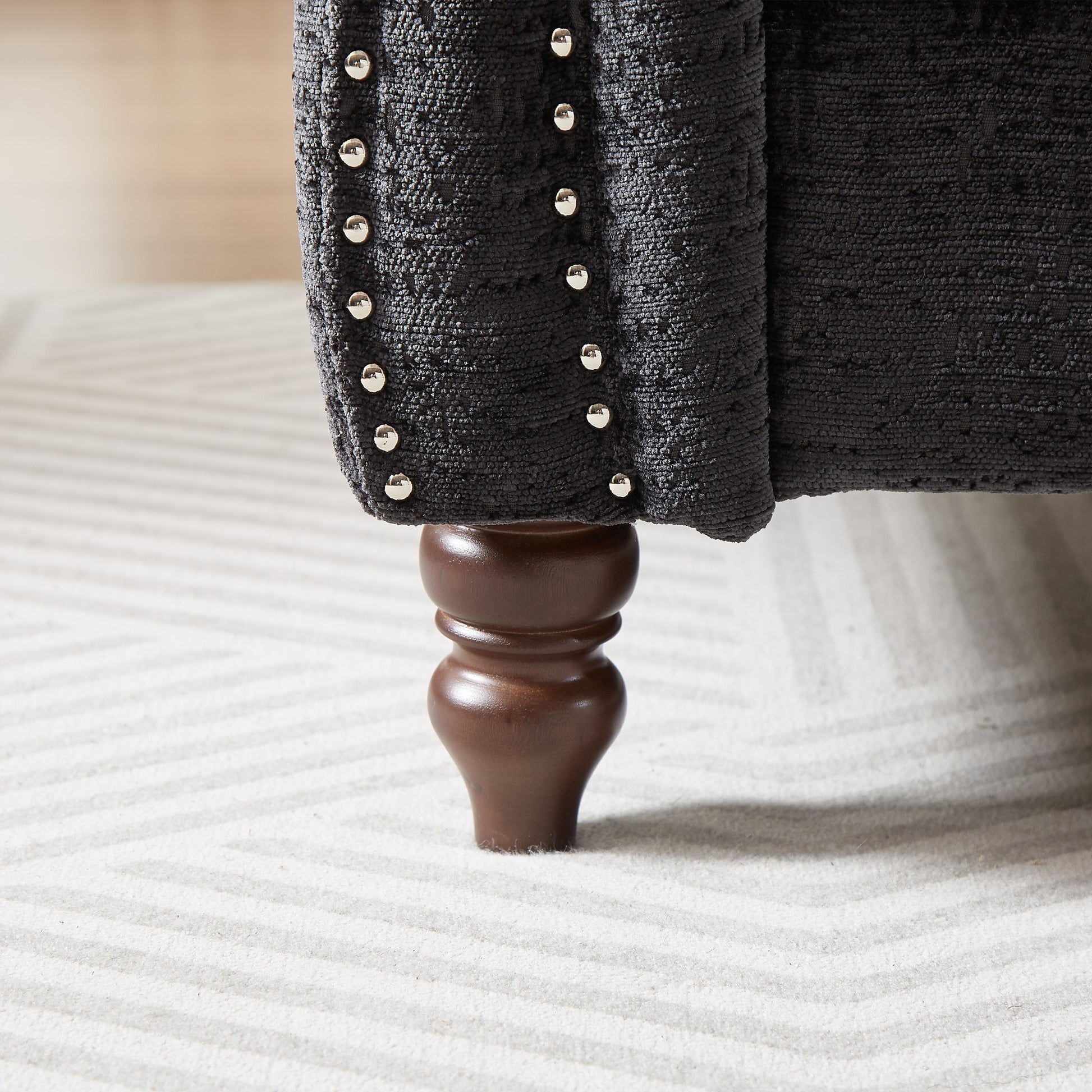 Dark grey textured upholstery armchair with silver nailhead trim and a carved wood leg