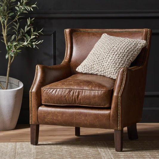 Distressed brown leather wingback armchair with nailhead trim and cream knit pillow