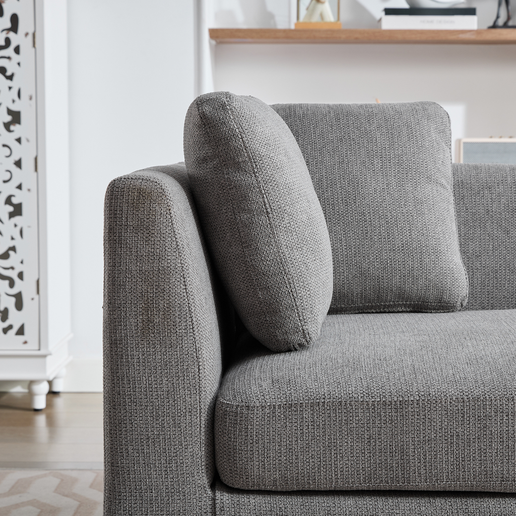 Closeup of a textured grey fabric sofa armrest with two plush throw pillows