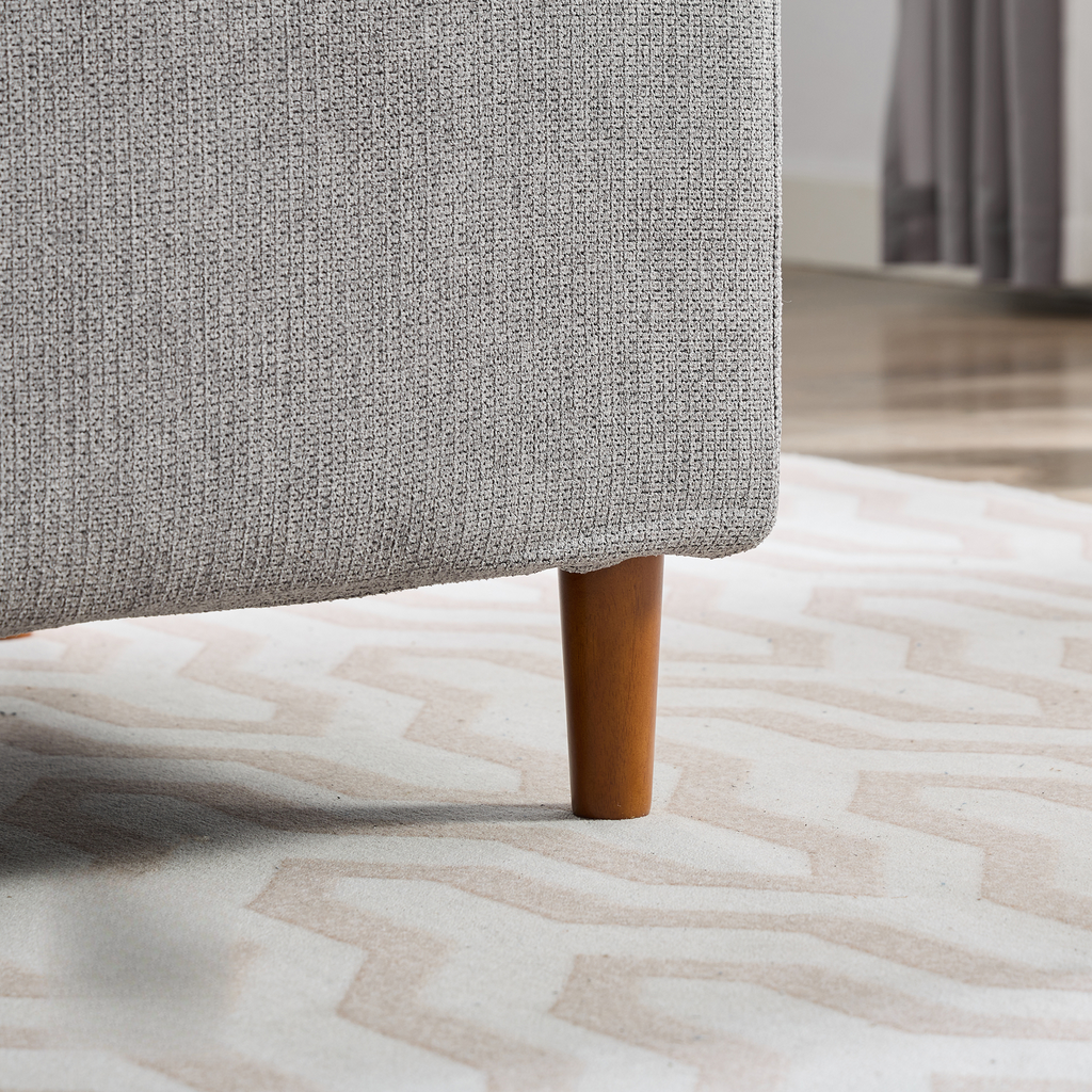 Closeup of a grey textured sofa leg with a tapered wooden foot on a geometric rug