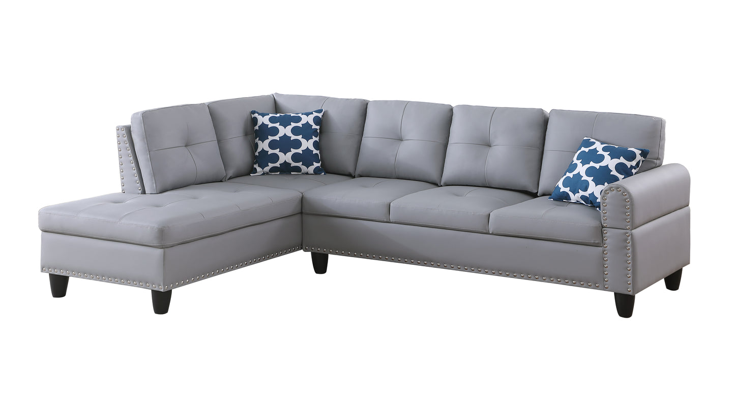Grey tufted faux leather sectional sofa with silver nailhead trim and blue patterned pillows