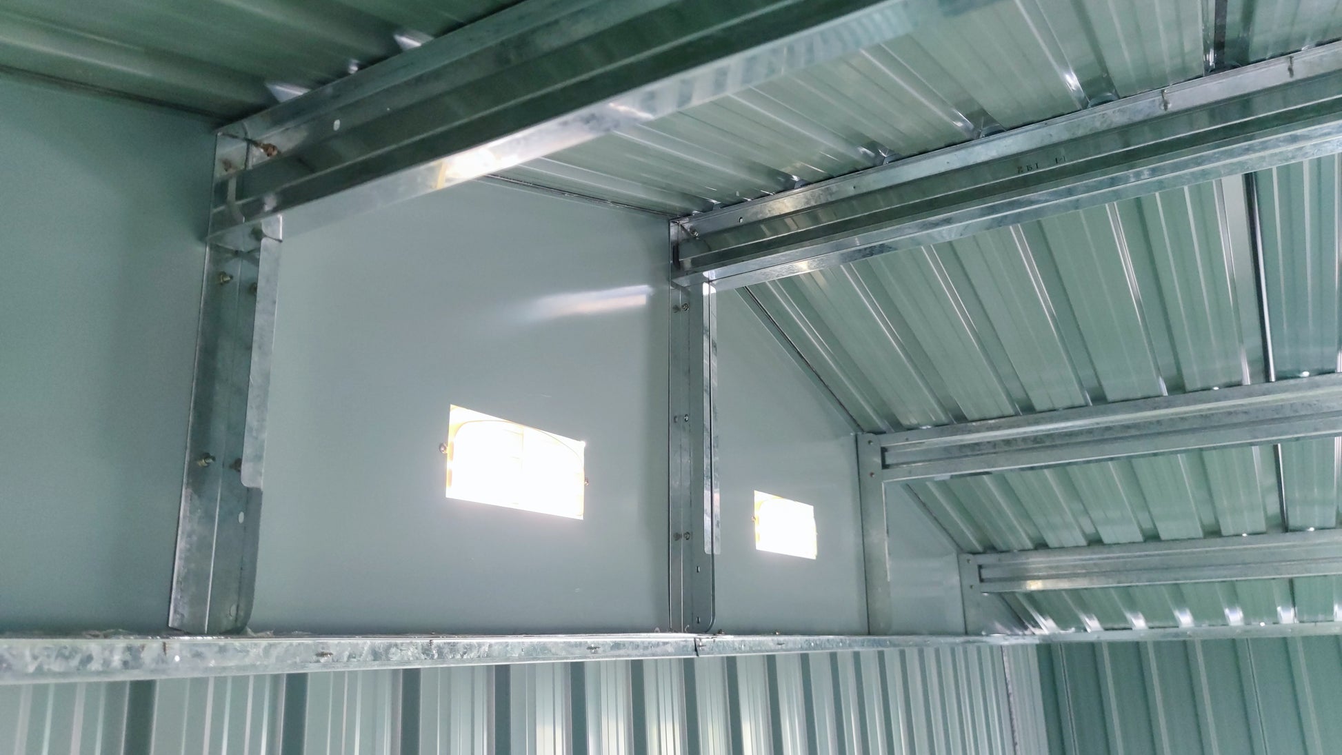 Green metal garden shed interior with corrugated roof and structural supports