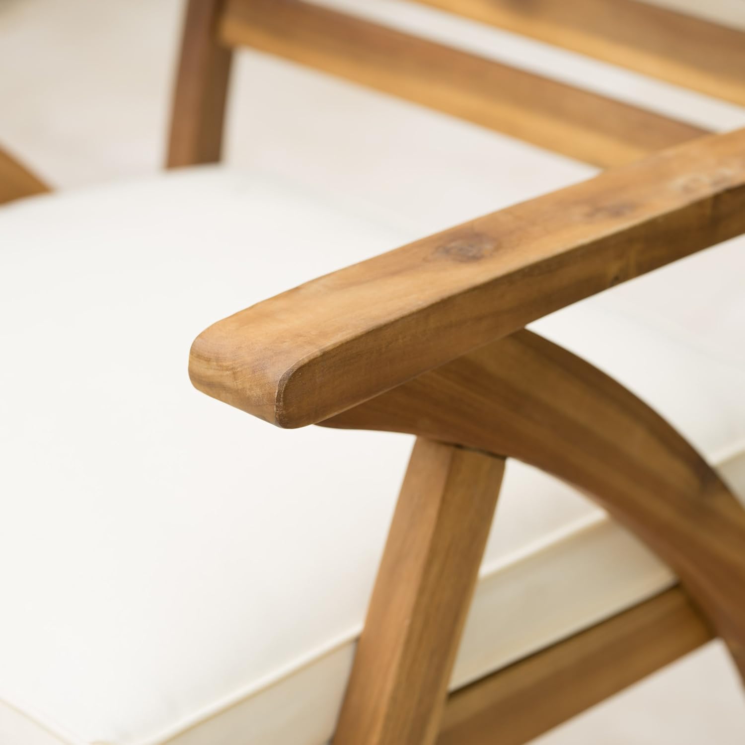 Closeup of a lightcolored cushion on a natural wood armchair with curved armrests