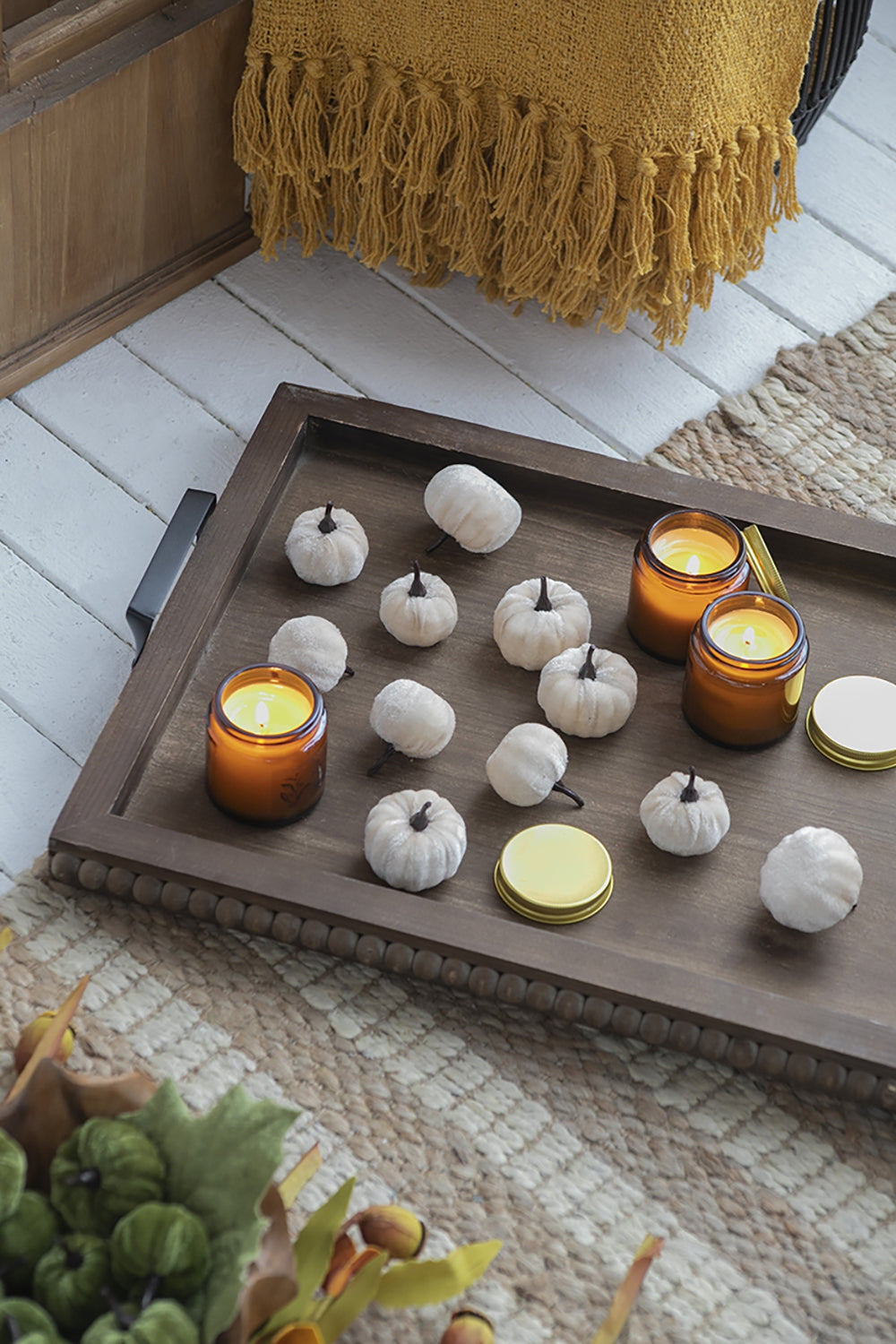 Set of  plush white pumpkins with dark stems arranged on a wooden tray with candles