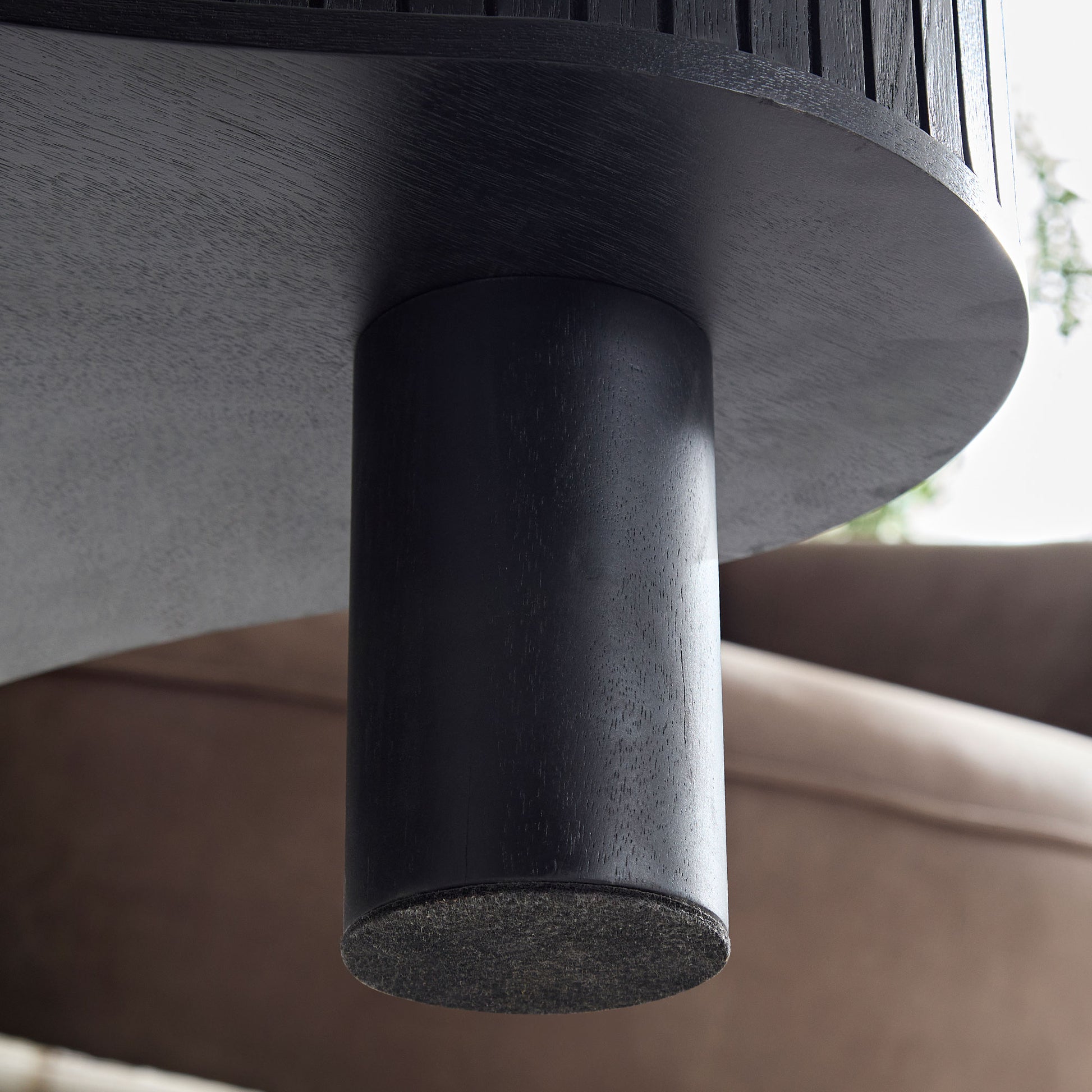 Close up of a dark wood round table leg with felt protector