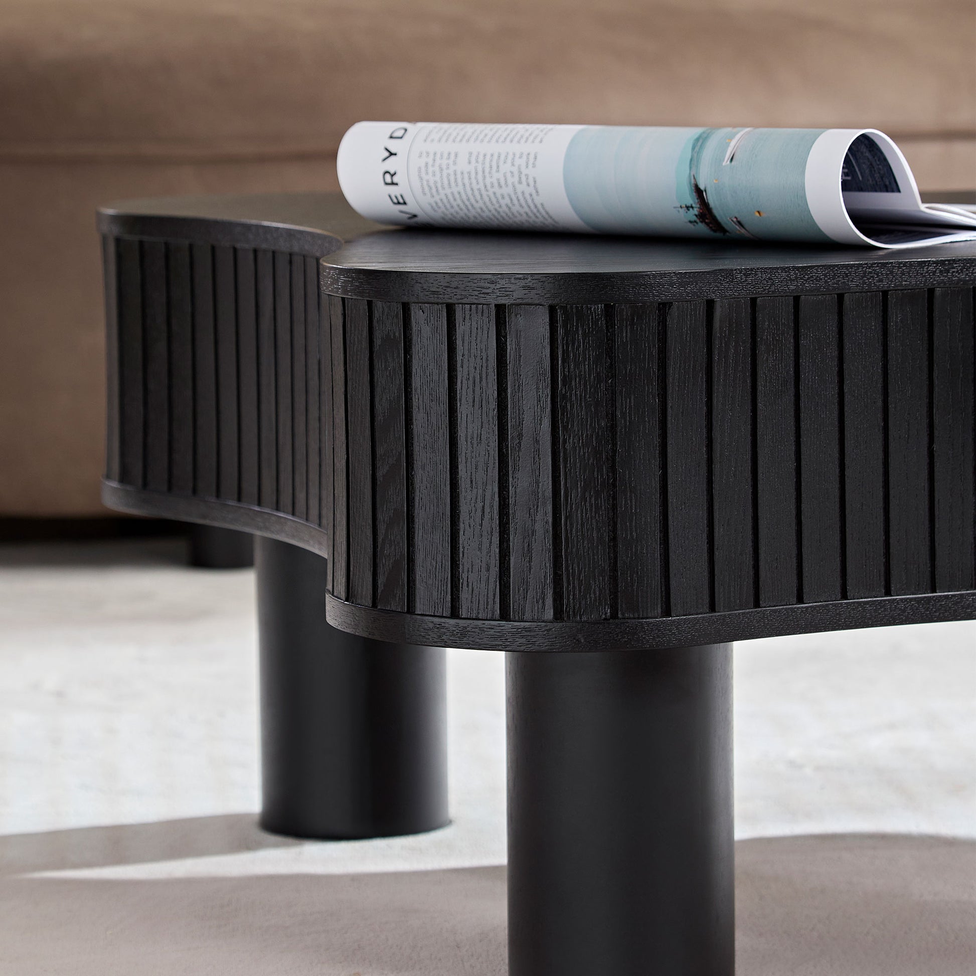 Black fluted wood coffee table with curved edges featuring a magazine detail