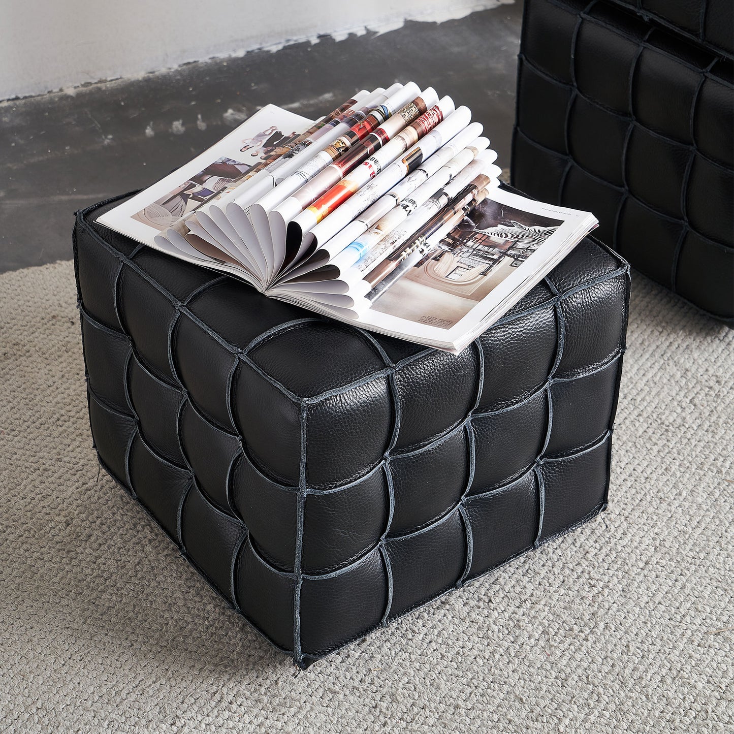 Black leather ottoman with a woven design and magazines on top