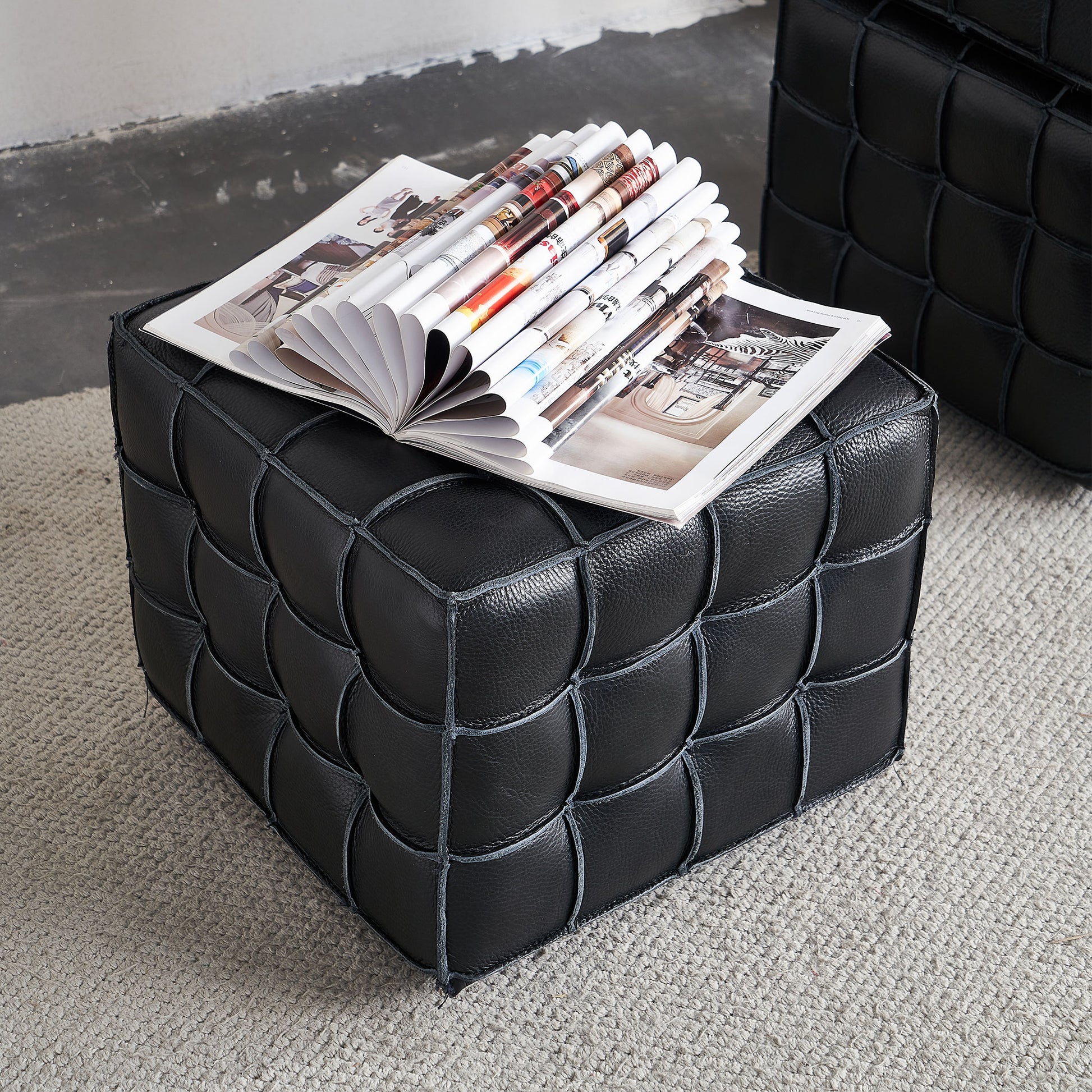 Black leather ottoman with a woven design and magazines on top
