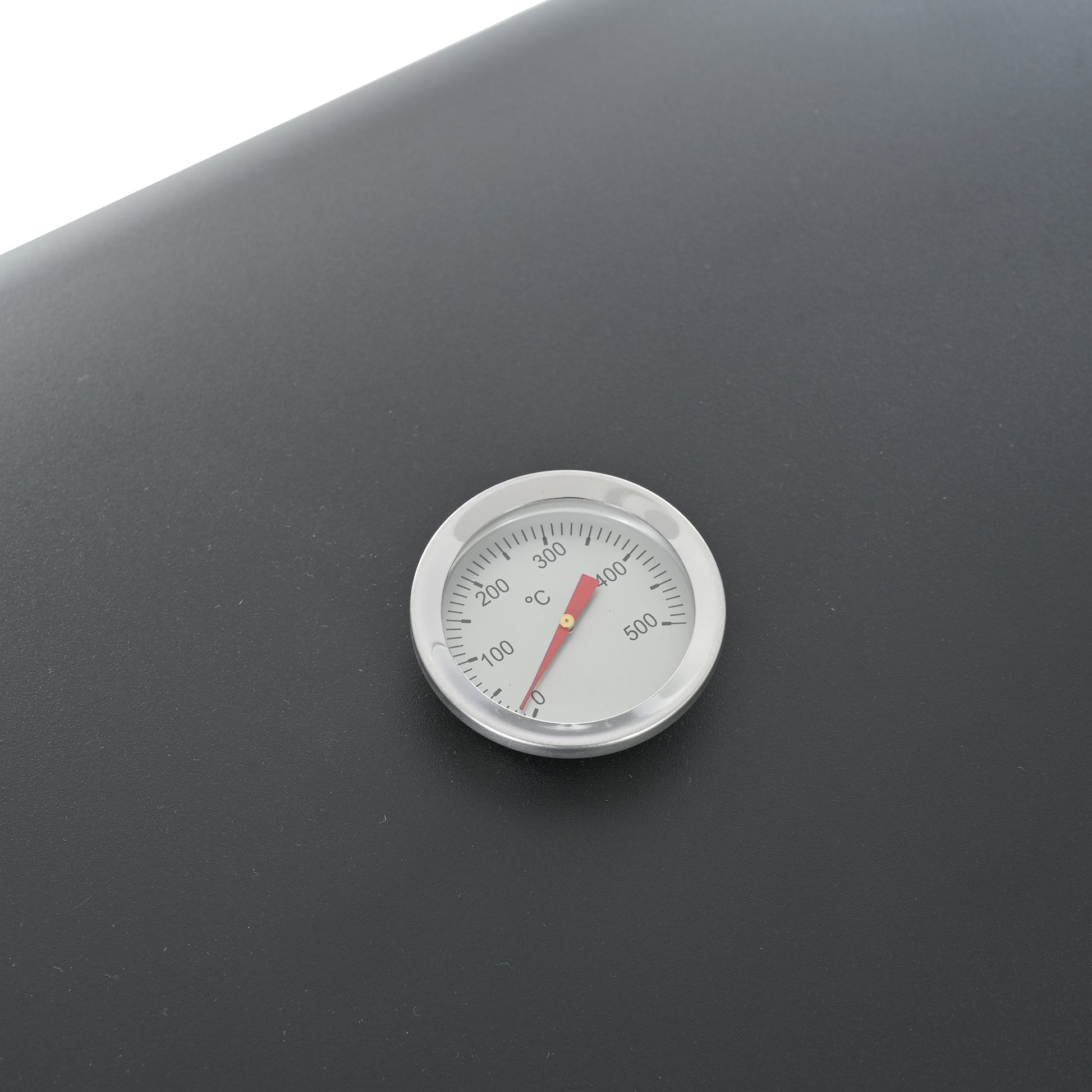 Closeup of a builtin thermometer showing  degrees Fahrenheit on a black grill lid