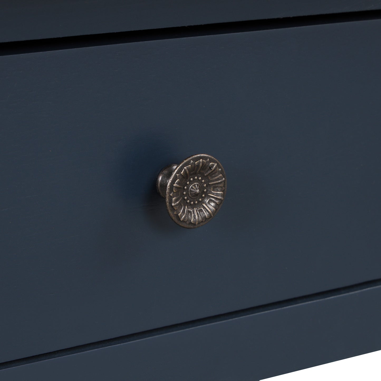 Closeup of an antique bronze drawer pull with floral detailing on a navy blue cabinet