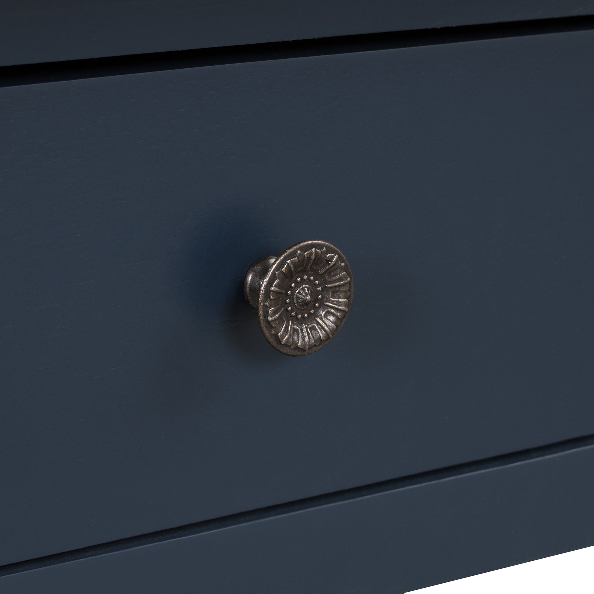Closeup of an antique bronze drawer pull with floral detailing on a navy blue cabinet