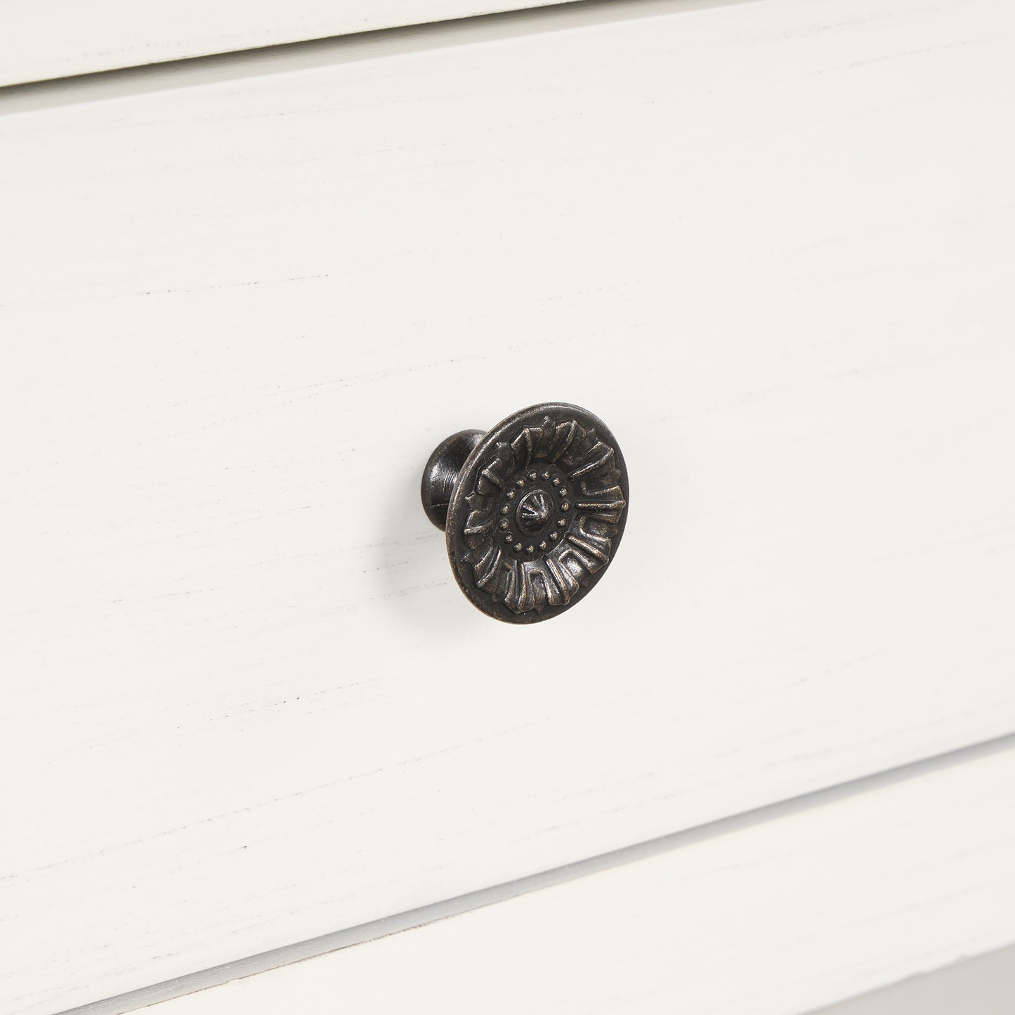 Antique brass ornate drawer knob with floral detail on white wood