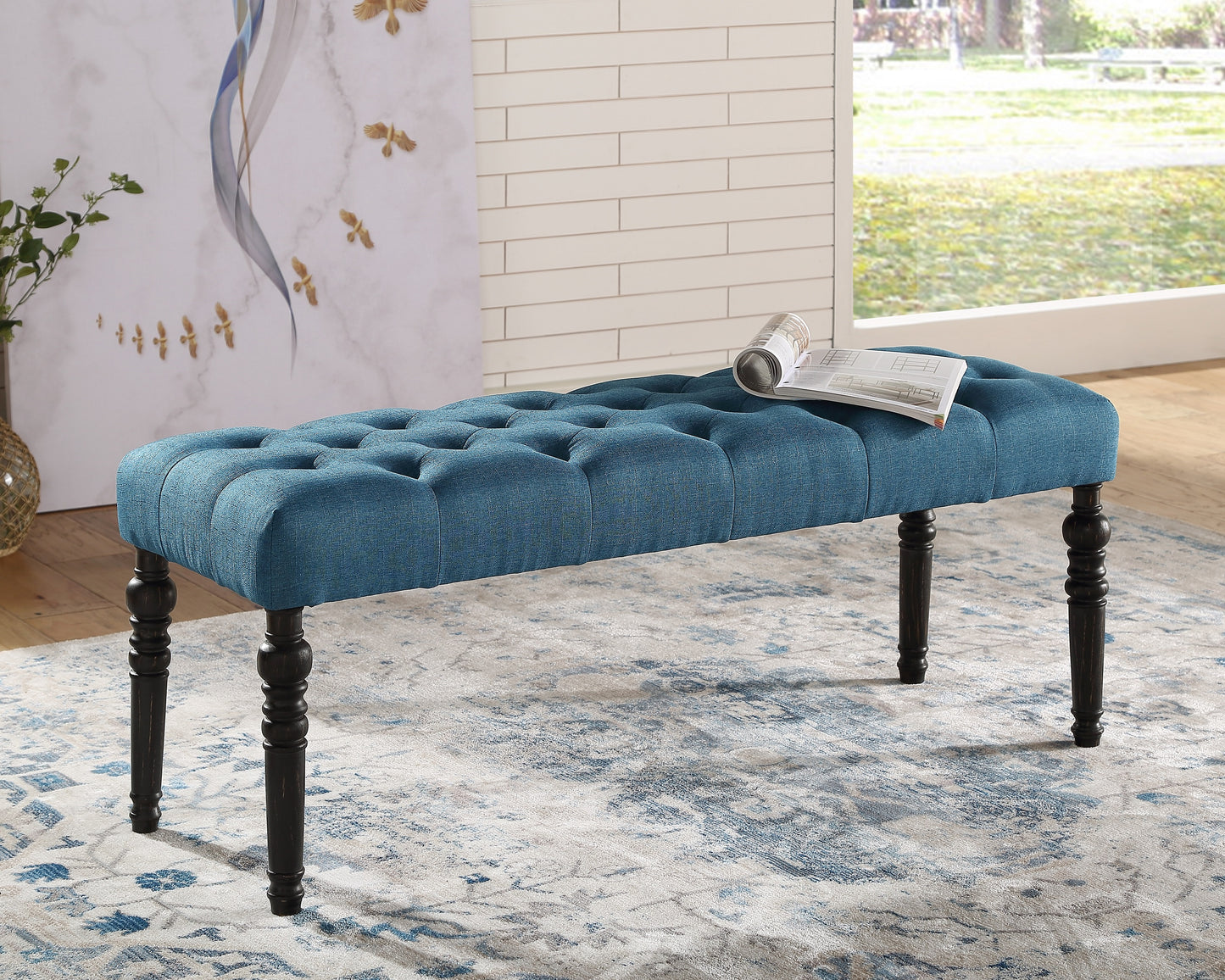 Tufted teal fabric bench with dark wood carved legs and a rolled magazine on top