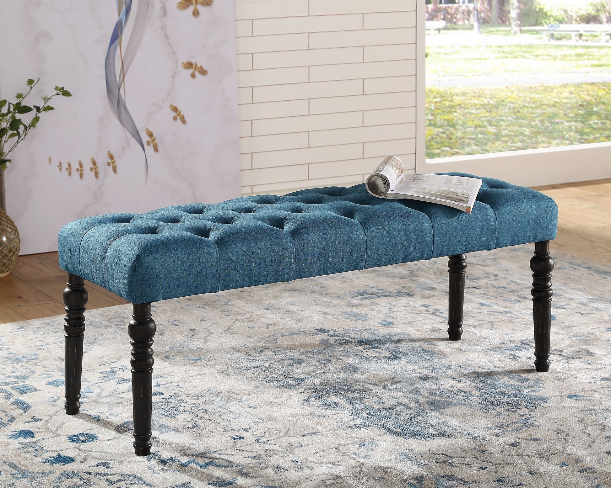 Tufted teal fabric bench with dark wood carved legs and a rolled magazine on top