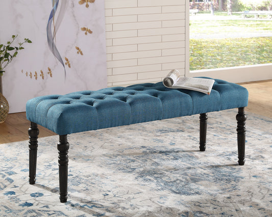 Tufted teal fabric bench with dark wood carved legs and a rolled magazine on top
