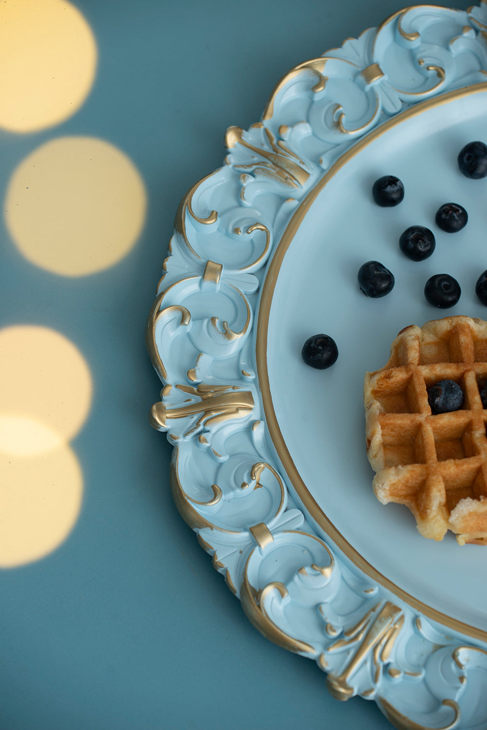 Light blue ornate serving platter with gold trim holding waffles and blueberries