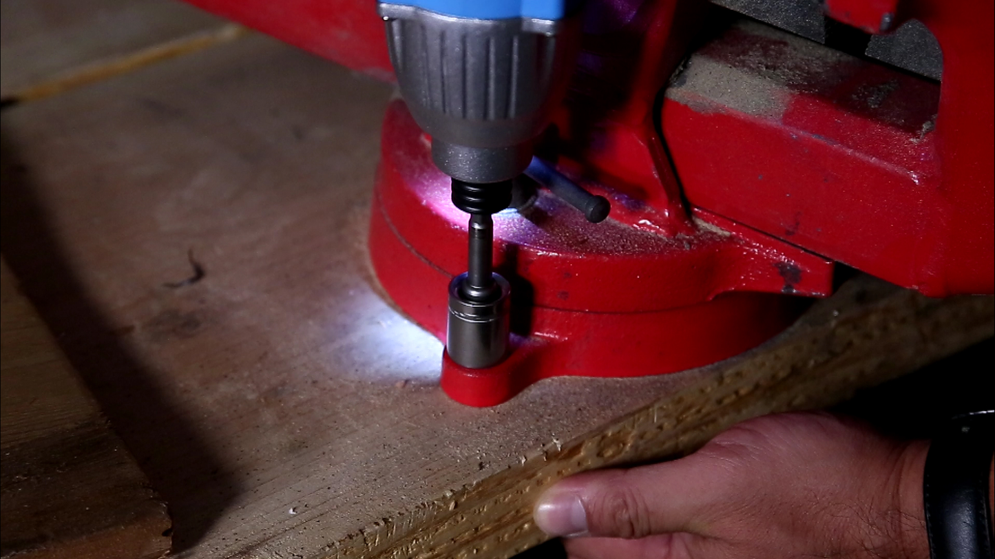 Impact driver with LED light secures a screw into a red vise holding particle board