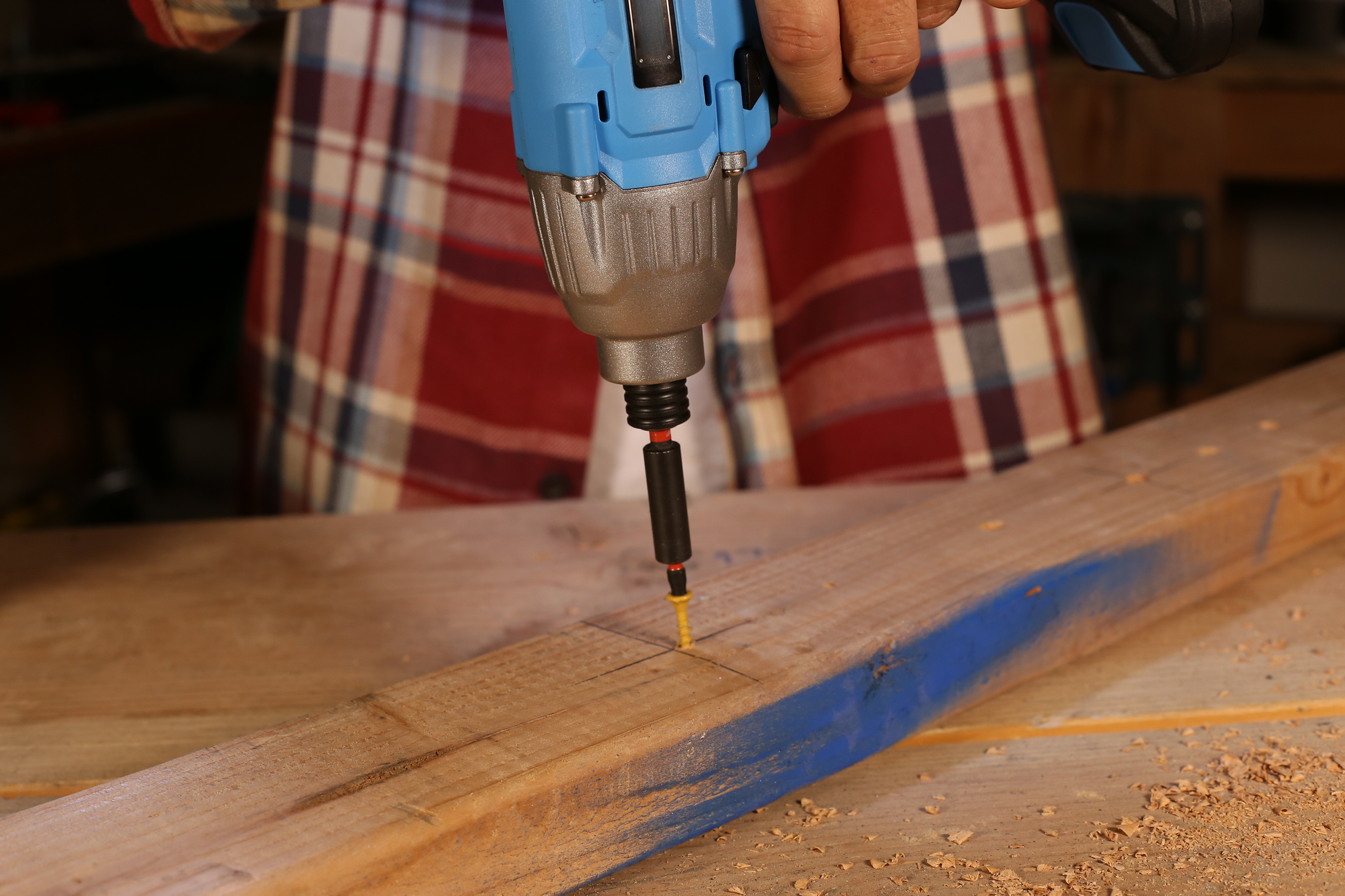 Blue and silver cordless impact driver screwing yellow wood screw into pine board