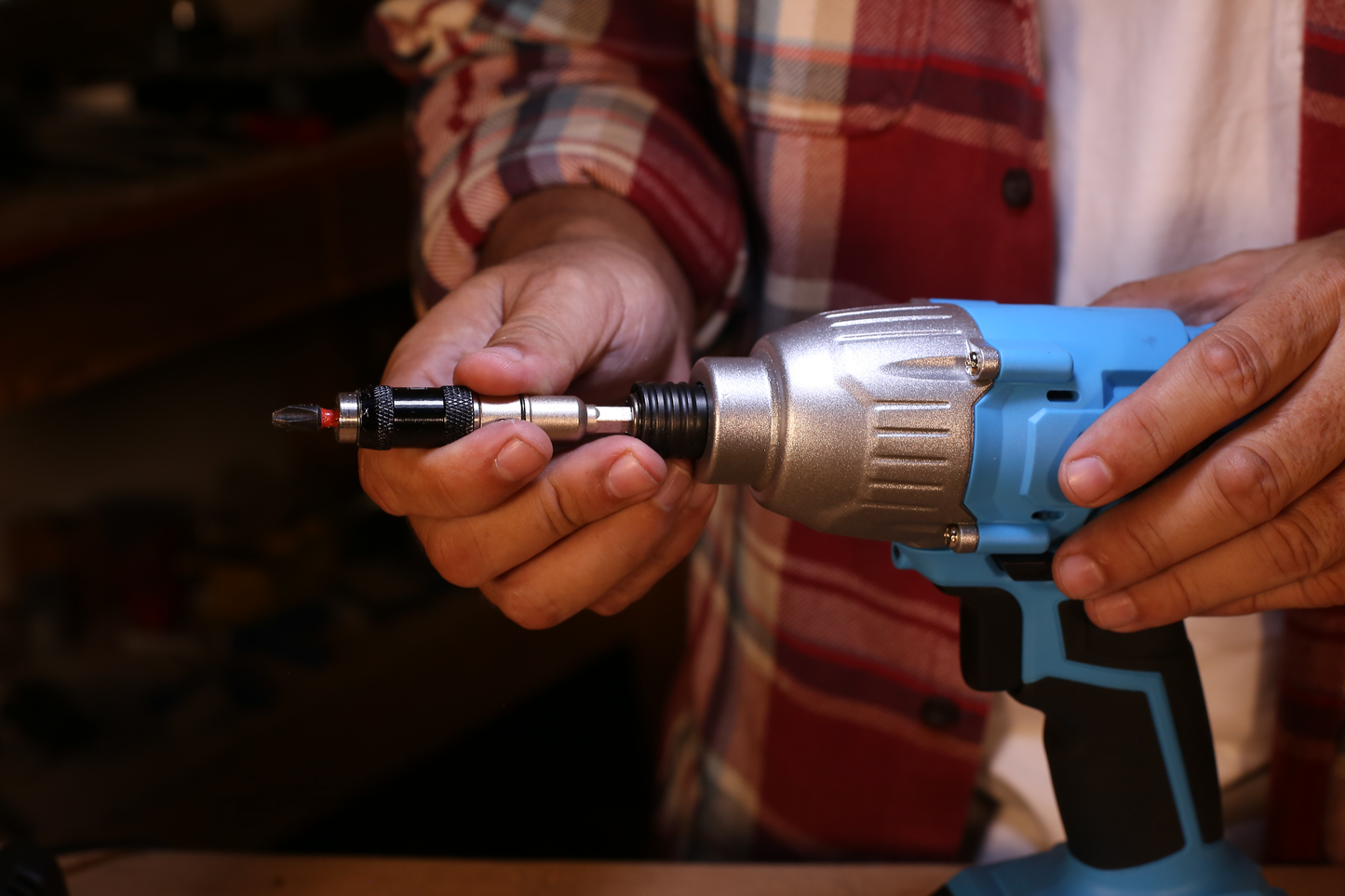 Closeup of a persons hands holding a blue impact driver with a bit attached