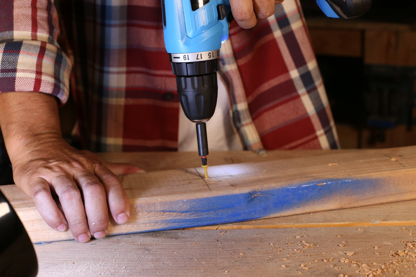 Blue cordless drill driving a yellow screw into a wooden plank