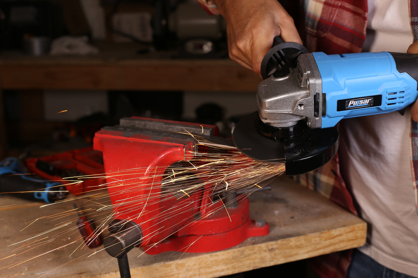 Blue angle grinder sparks flying while cutting metal held in a red vise