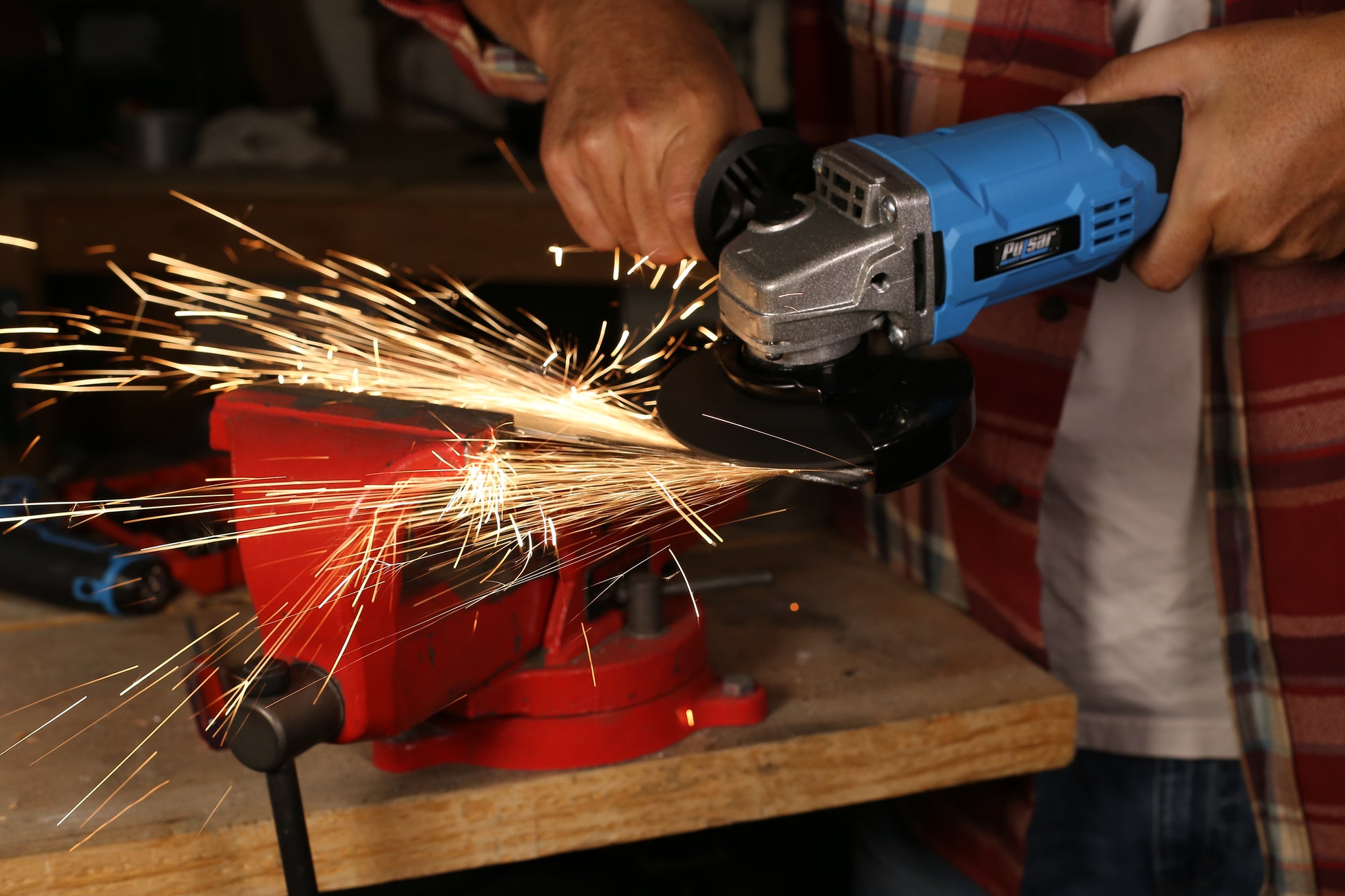 Blue Pulsar angle grinder sparks while cutting metal held in a red vise