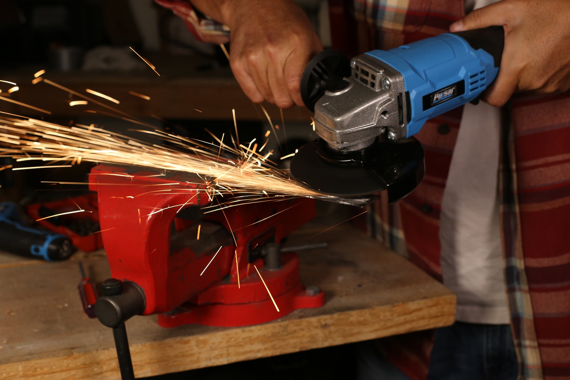 Blue cordless angle grinder cutting metal creating sparks against a red vise