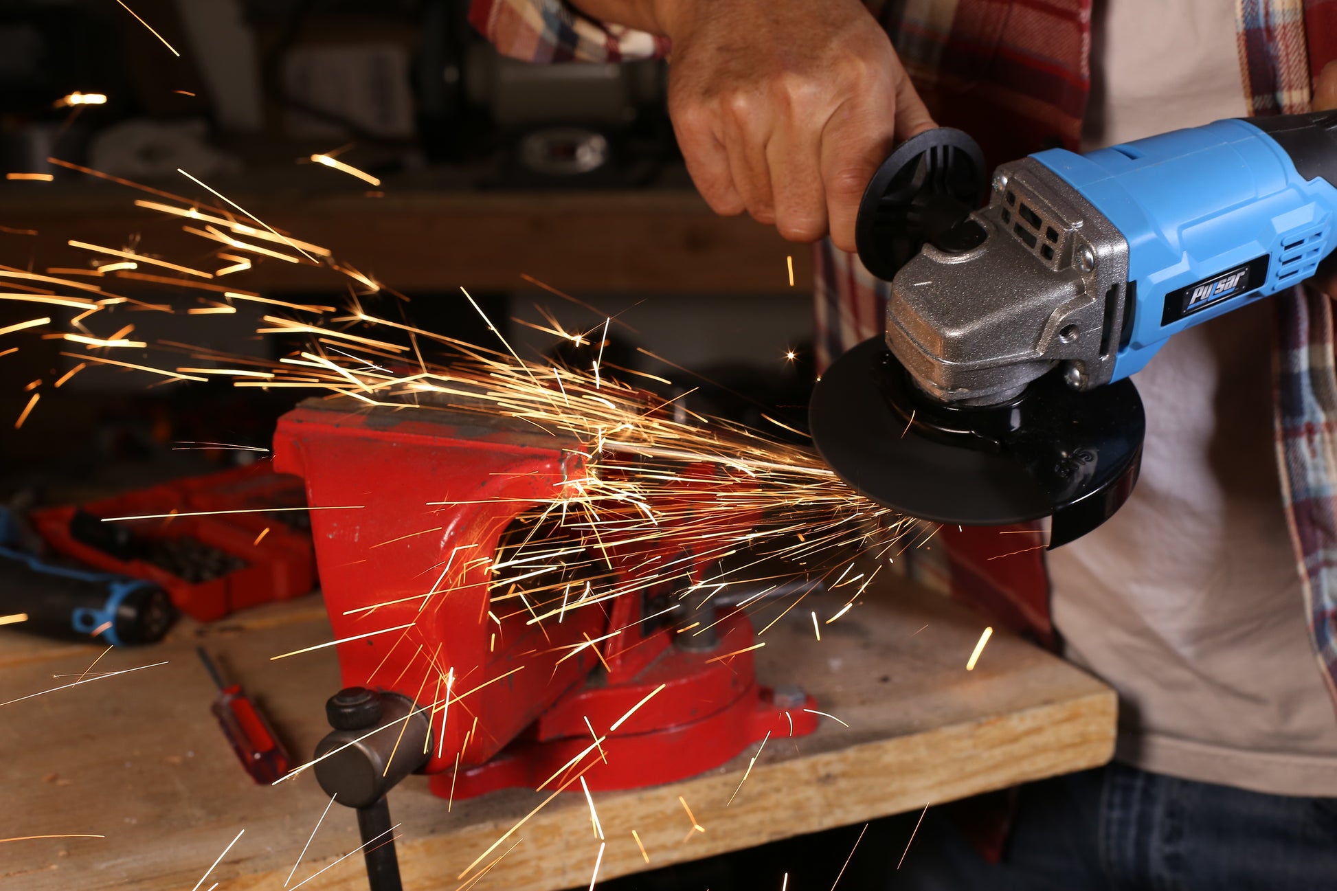 Blue angle grinder in action creating sparks while cutting metal clamped in a red vise
