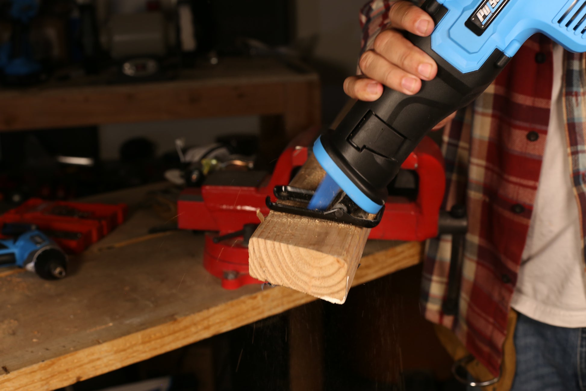 Blue and black reciprocating saw cutting a wooden plank dust flying