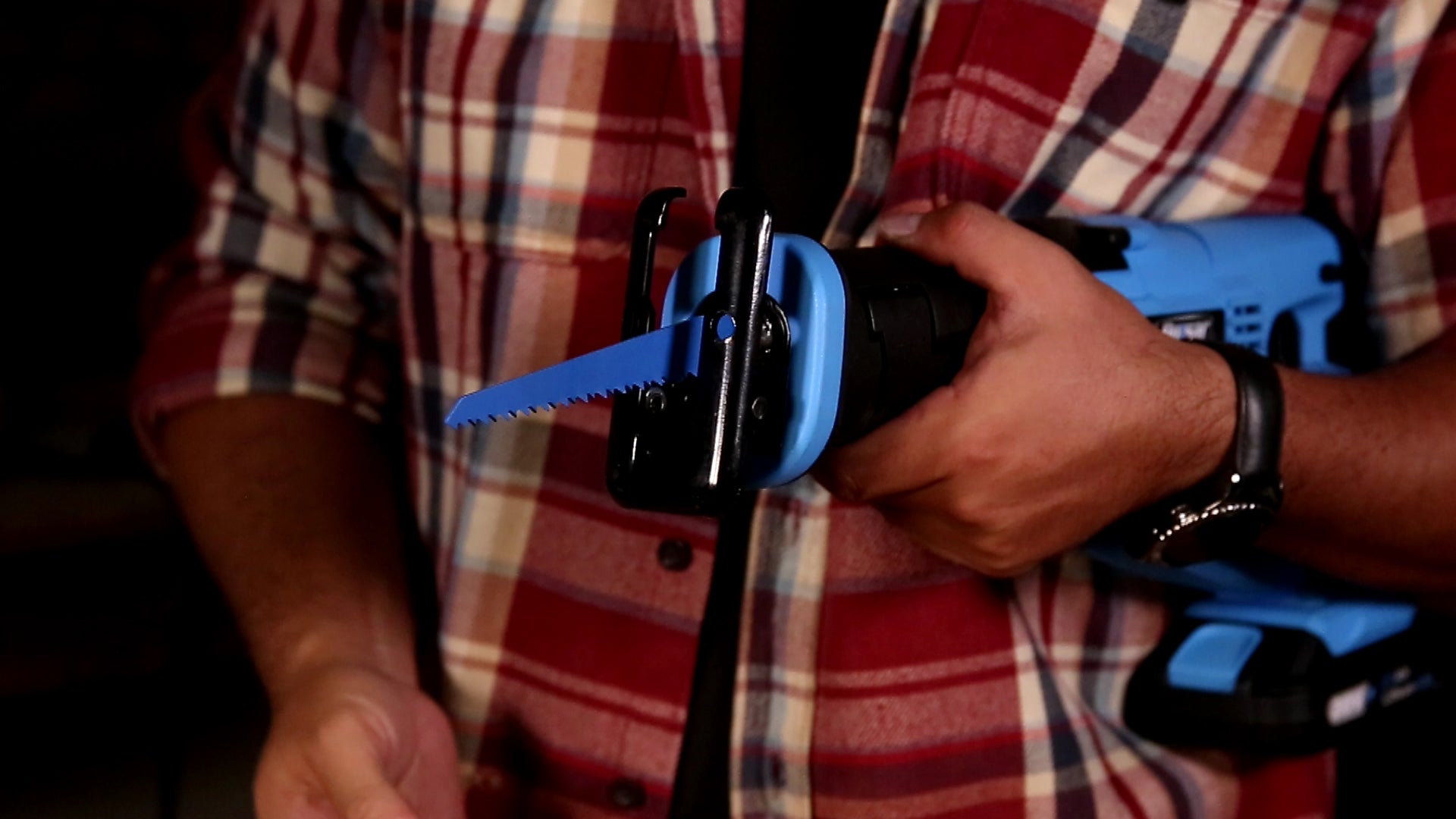Blue reciprocating saw with blue blade held by person in plaid shirt