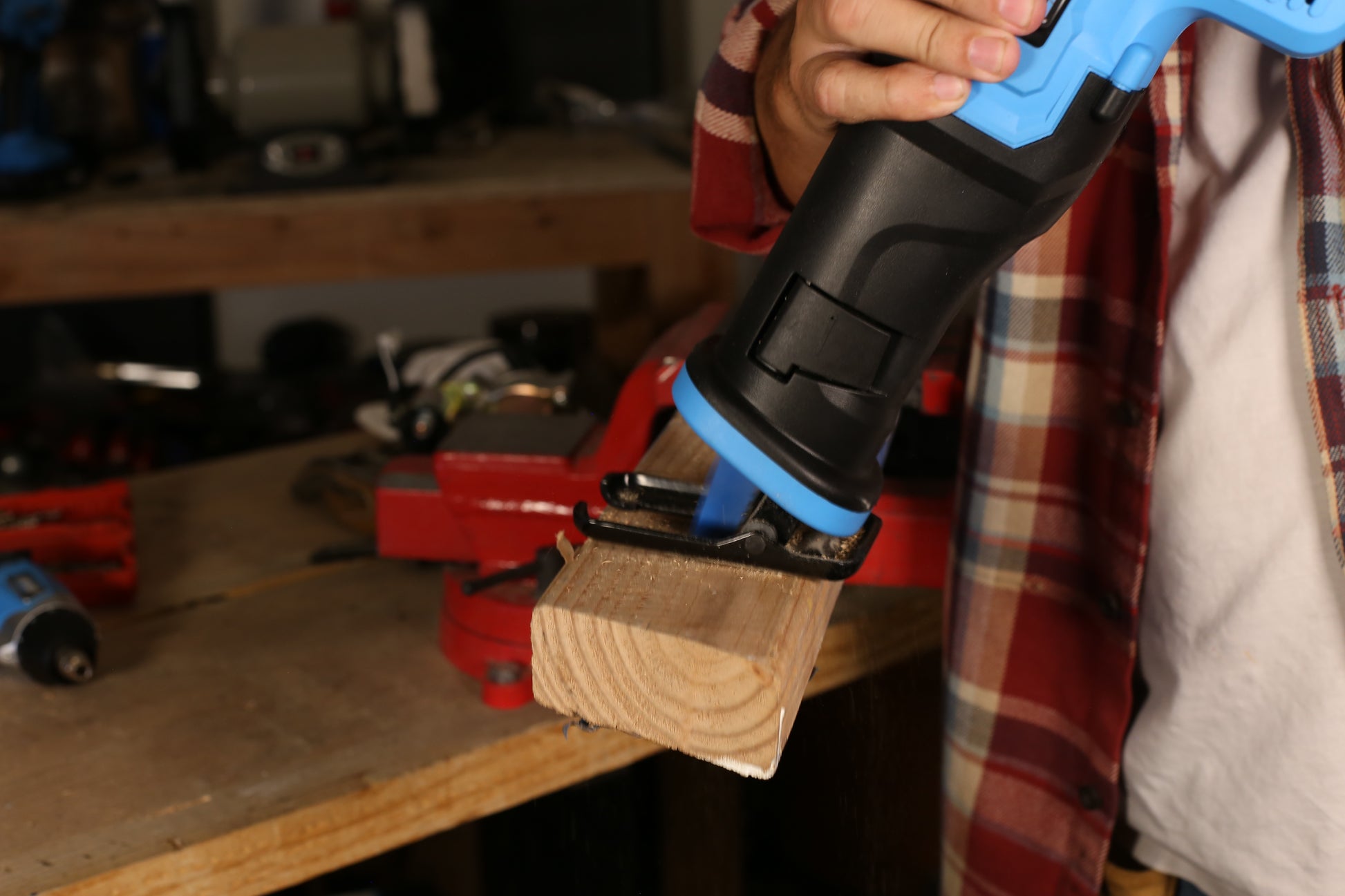 Blue and black reciprocating saw cutting a wooden plank held in a red vise