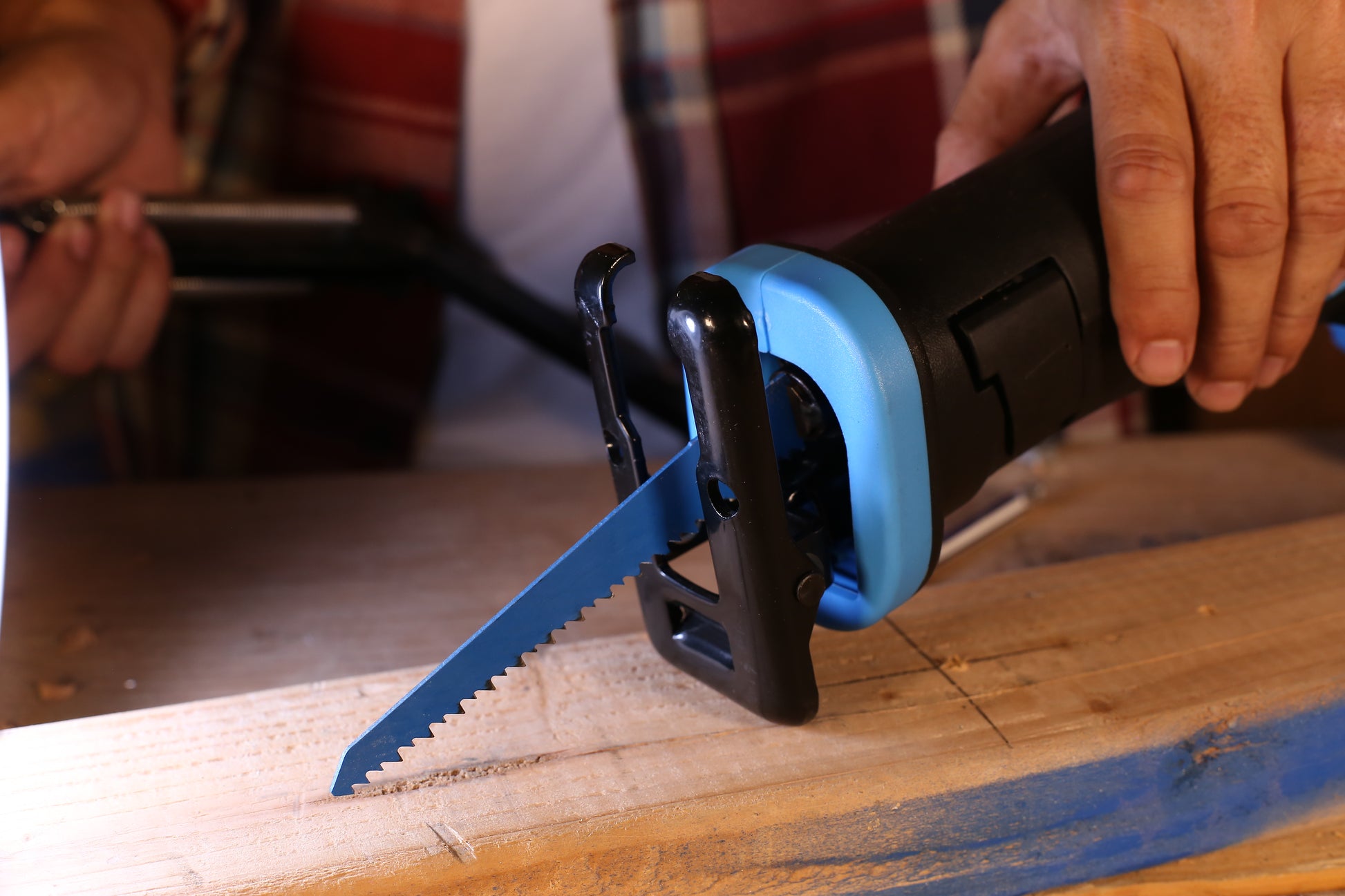 Black and blue reciprocating saw cutting through wood with a sharp blade