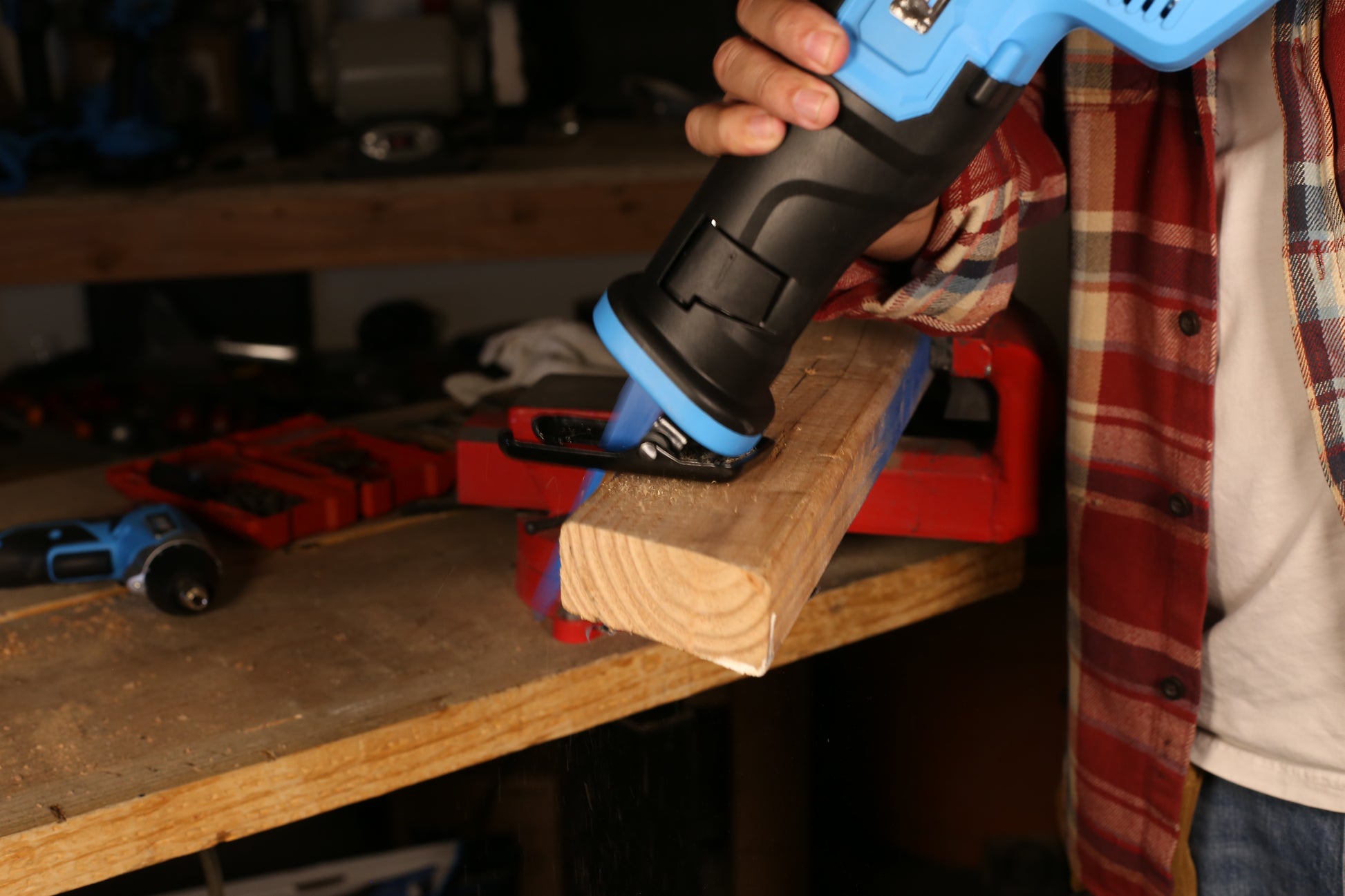 Blue and black reciprocating saw cutting a wooden beam held by a red vice