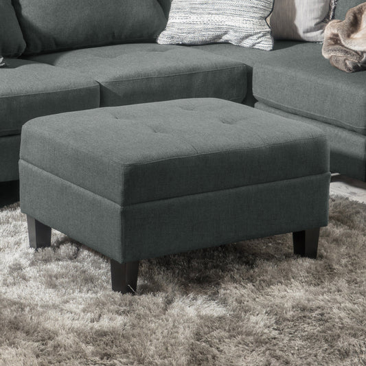 Tufted charcoal fabric ottoman with dark wood legs on a plush grey rug